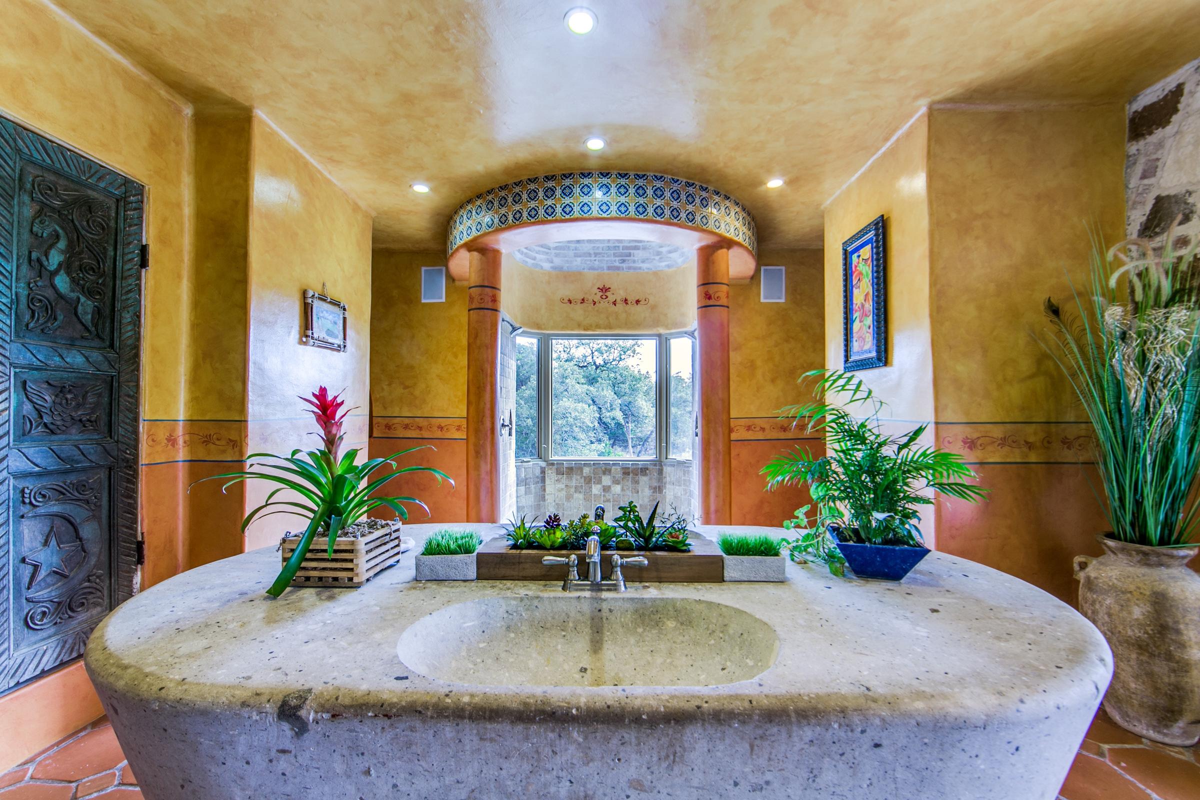 Luxurious Tuscan-style bathroom with stone basin sink, arched mosaic tile niche, and tropical plants in San Antonio, Texas