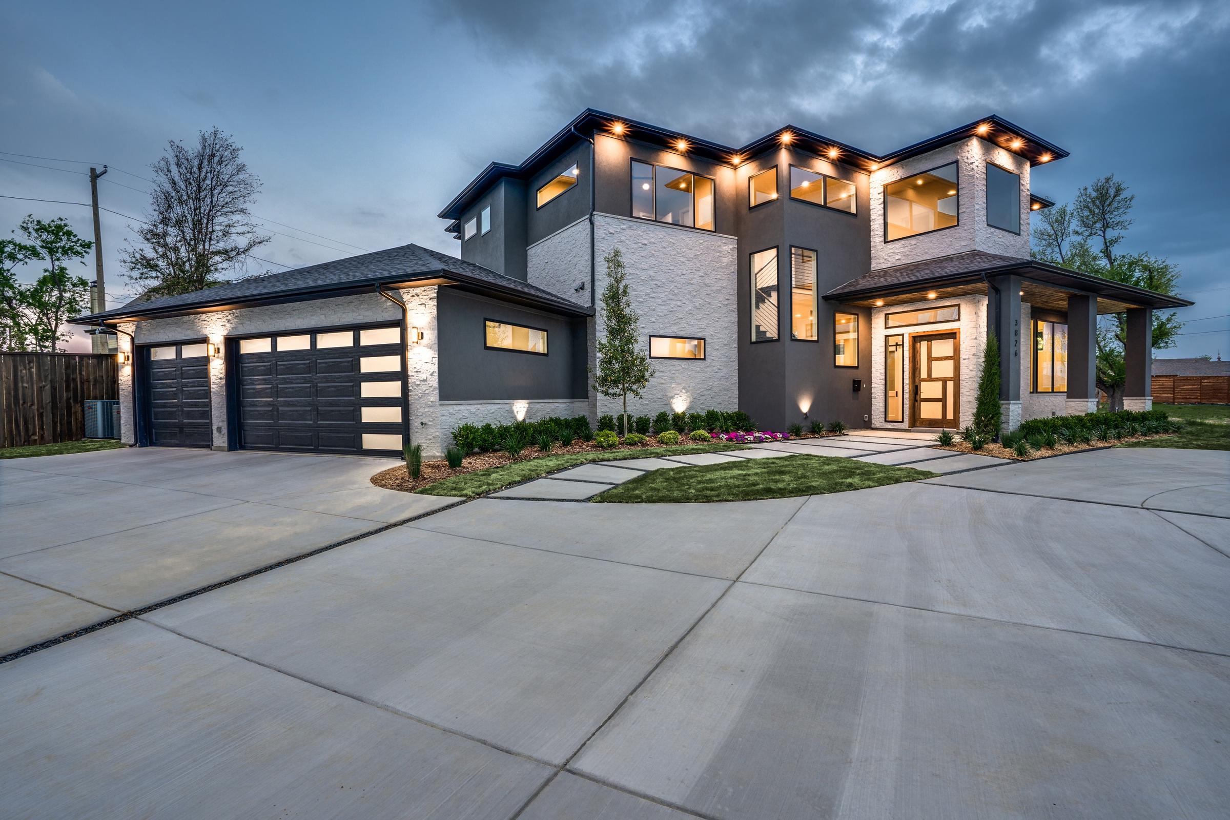Modern new construction home with warm interior glow, grey brick facade, and clean landscaping at twilight in Dallas, Texas