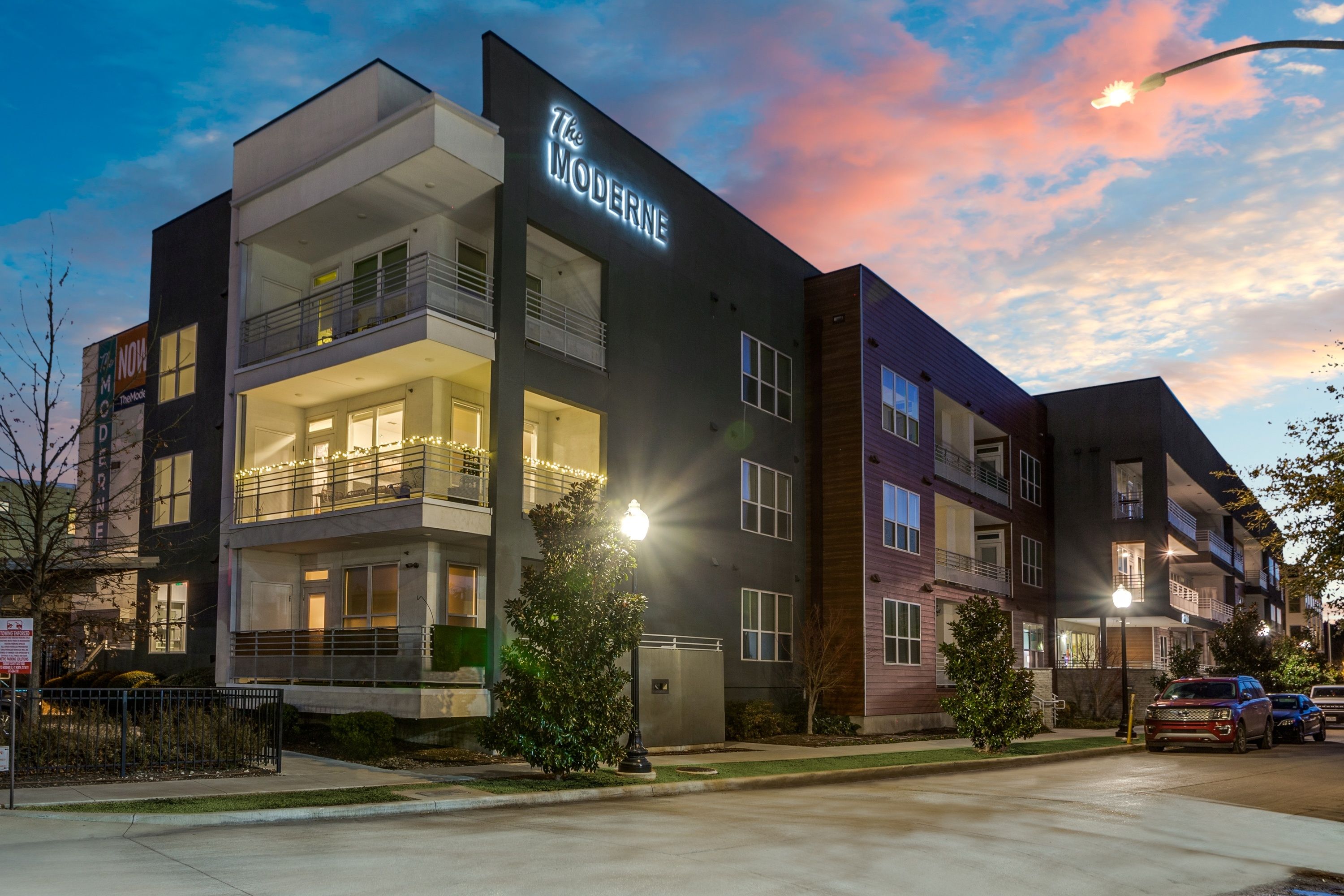 Modern three-story apartment building with illuminated balconies and warm window glow at twilight streetview in Fort Worth, Texas