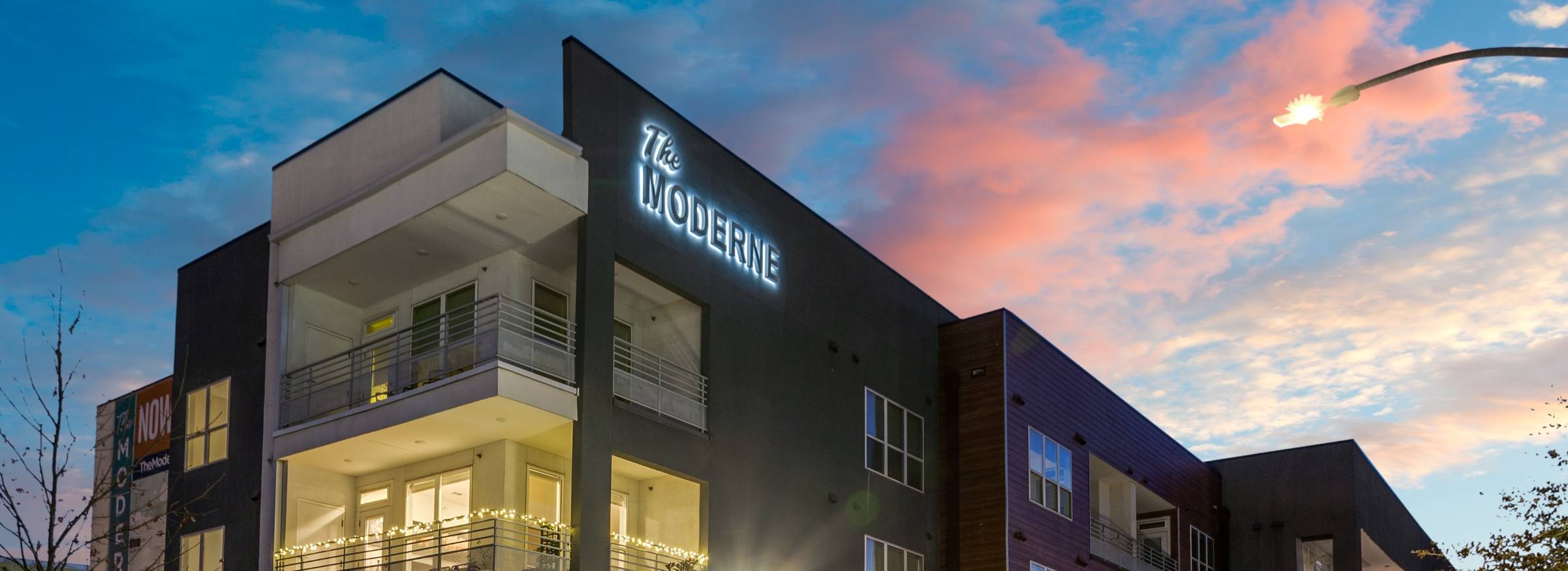 Modern three-story apartment building with illuminated balconies and warm window glow at twilight streetview in Fort Worth, Texas