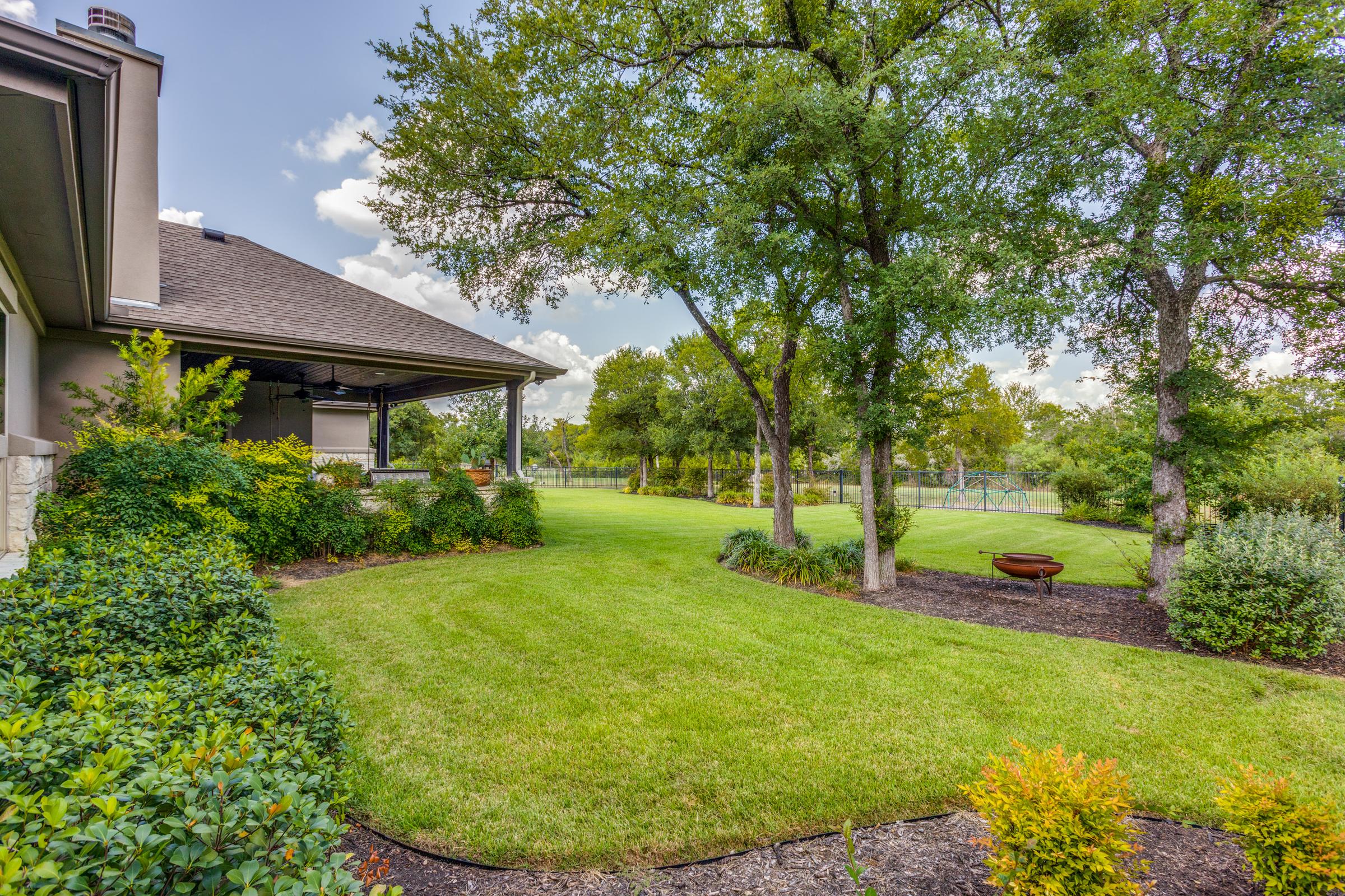 Large landscaped backyard with manicured lawn, mature trees, covered patio, and fire pit in Georgetown