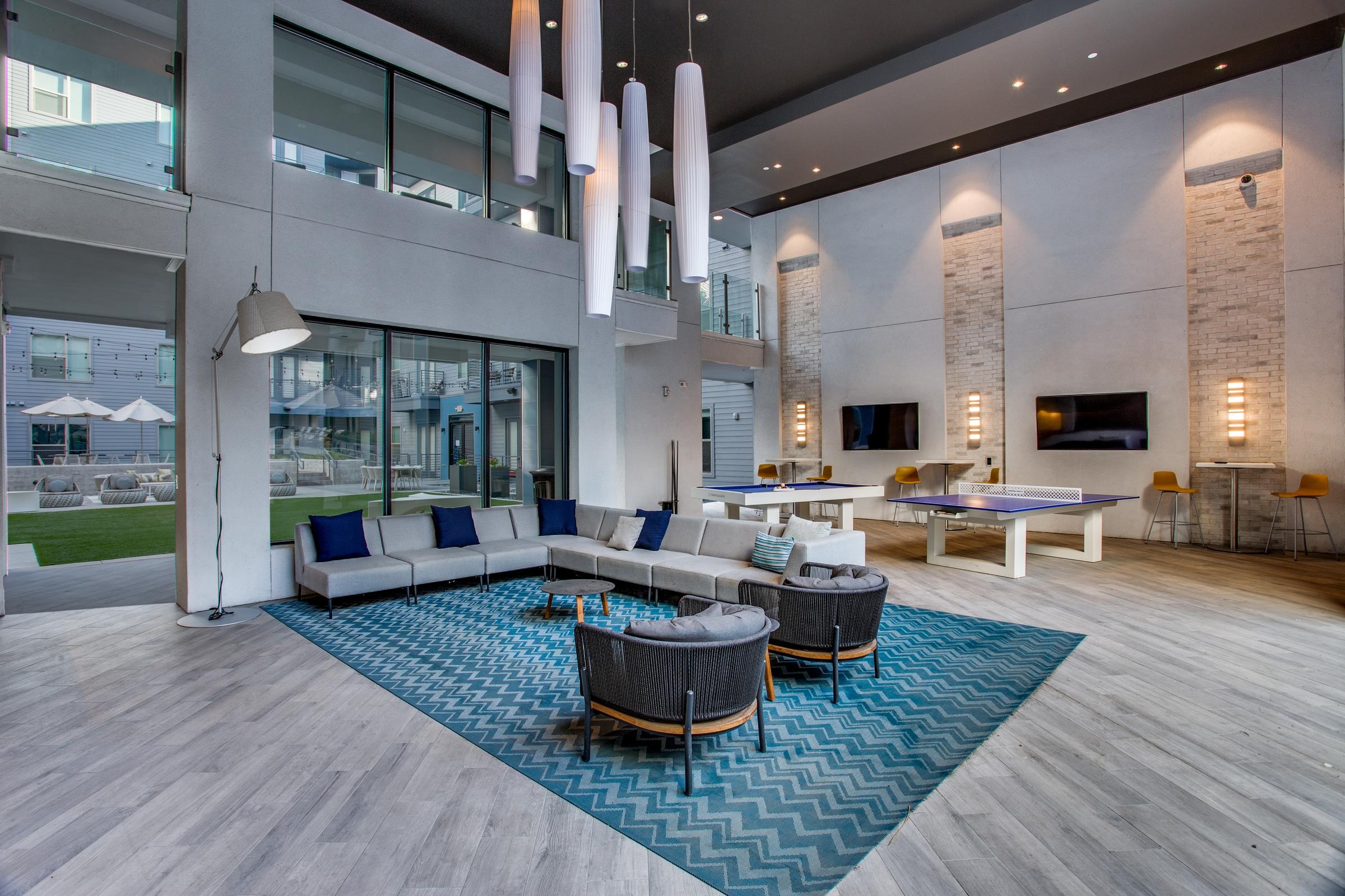 Modern apartment clubhouse with double-height ceilings, pendant lighting, lounge seating, and game area in Fort Worth, Texas