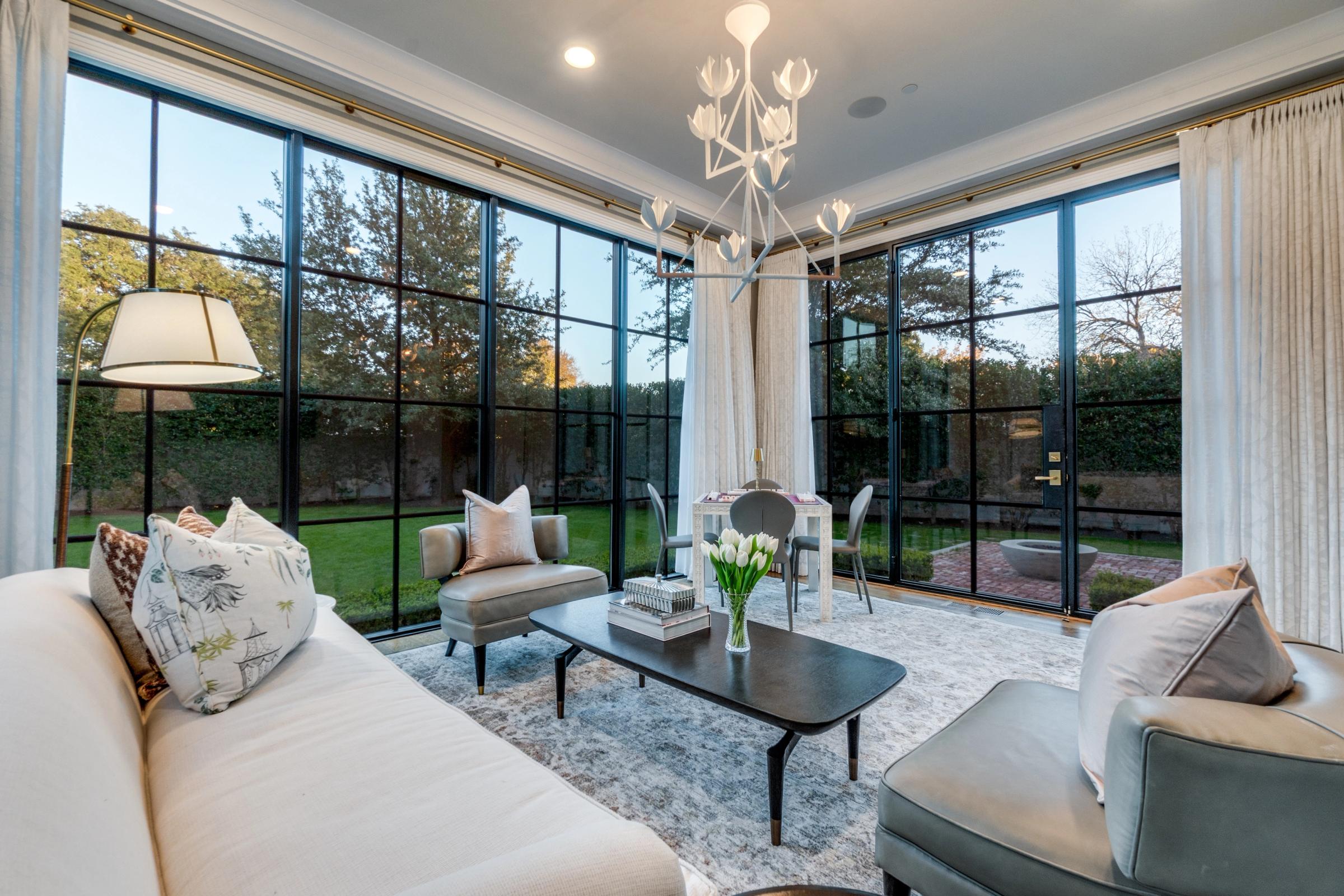 Elegant sunroom with floor-to-ceiling steel-frame windows, modern chandelier, and garden views in University Park, Texas