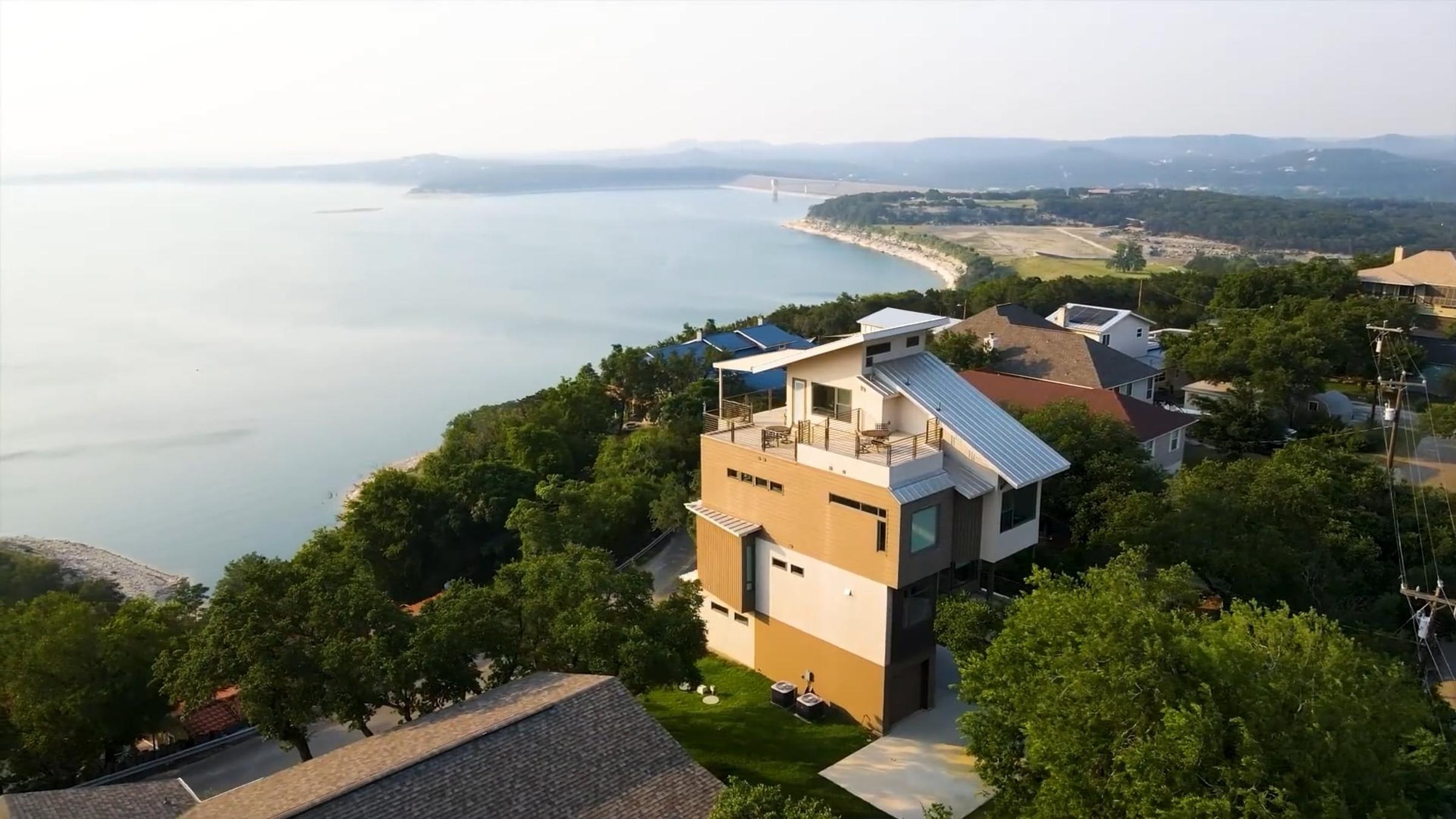 Aerial view of a modern lakefront home overlooking the lake with rolling hills in the background, Texas