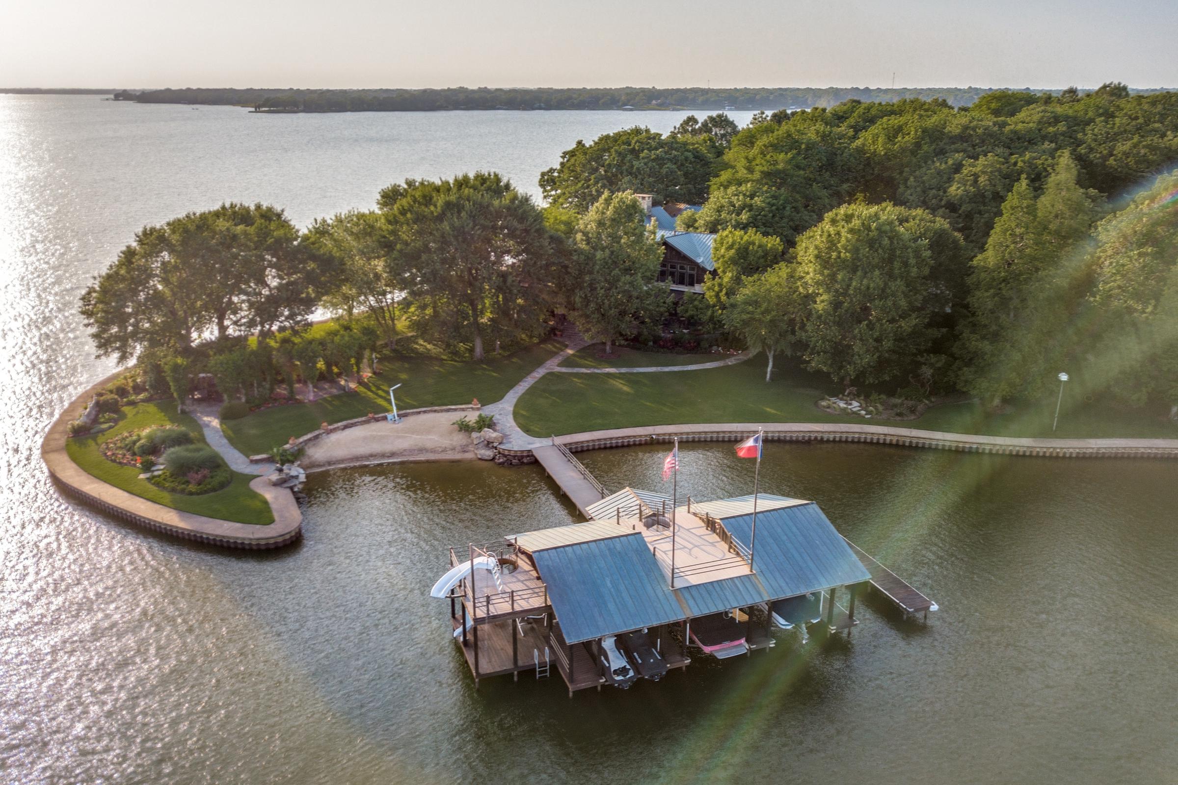 Aerial view of a lakefront luxury estate with two-story boat dock and Texas flag on Cedar Creek Lake in Malakoff, Texas