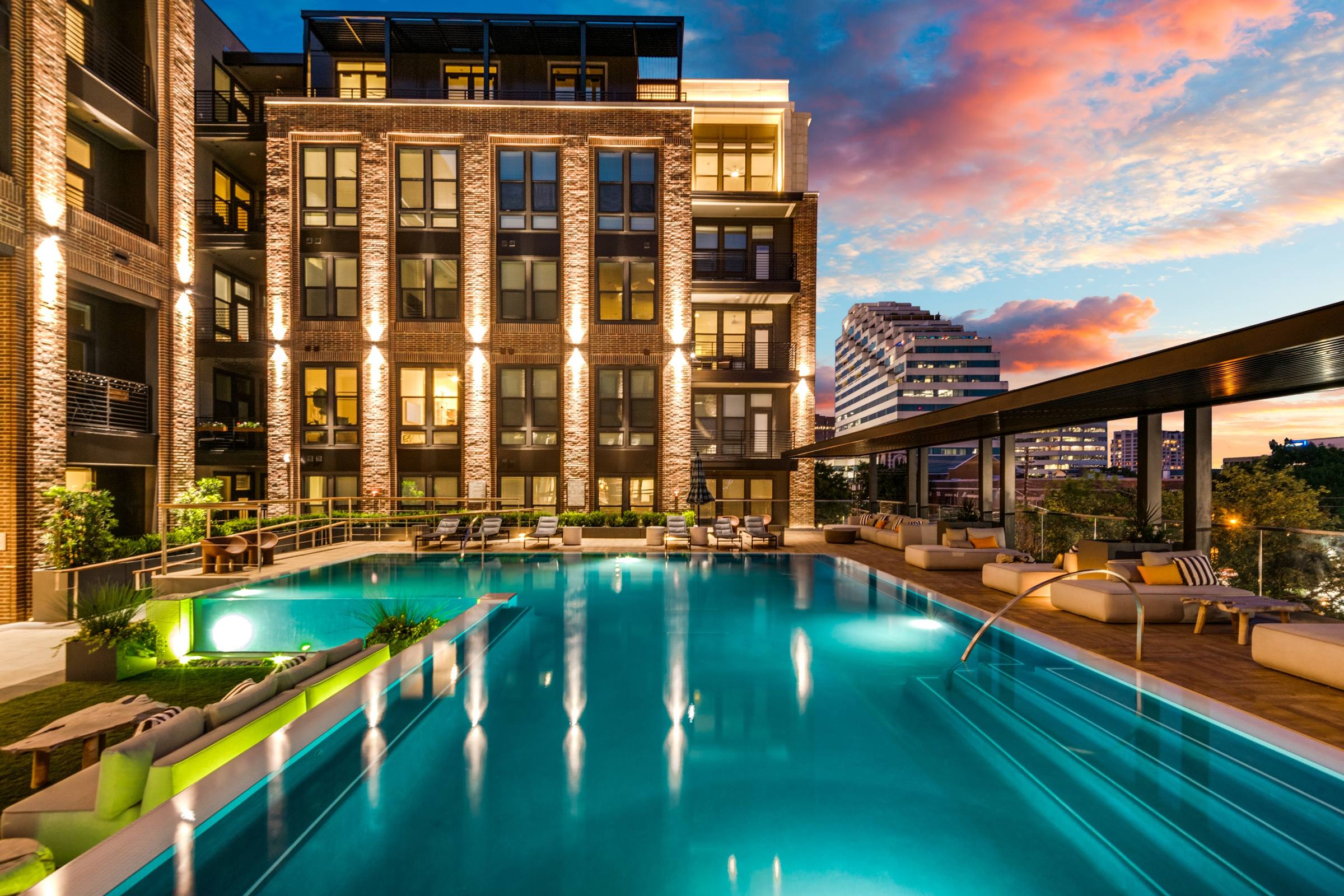Rooftop infinity pool at sunset with a brick mid-rise apartment building and Dallas skyline views in Oaklawn, Dallas, Texas