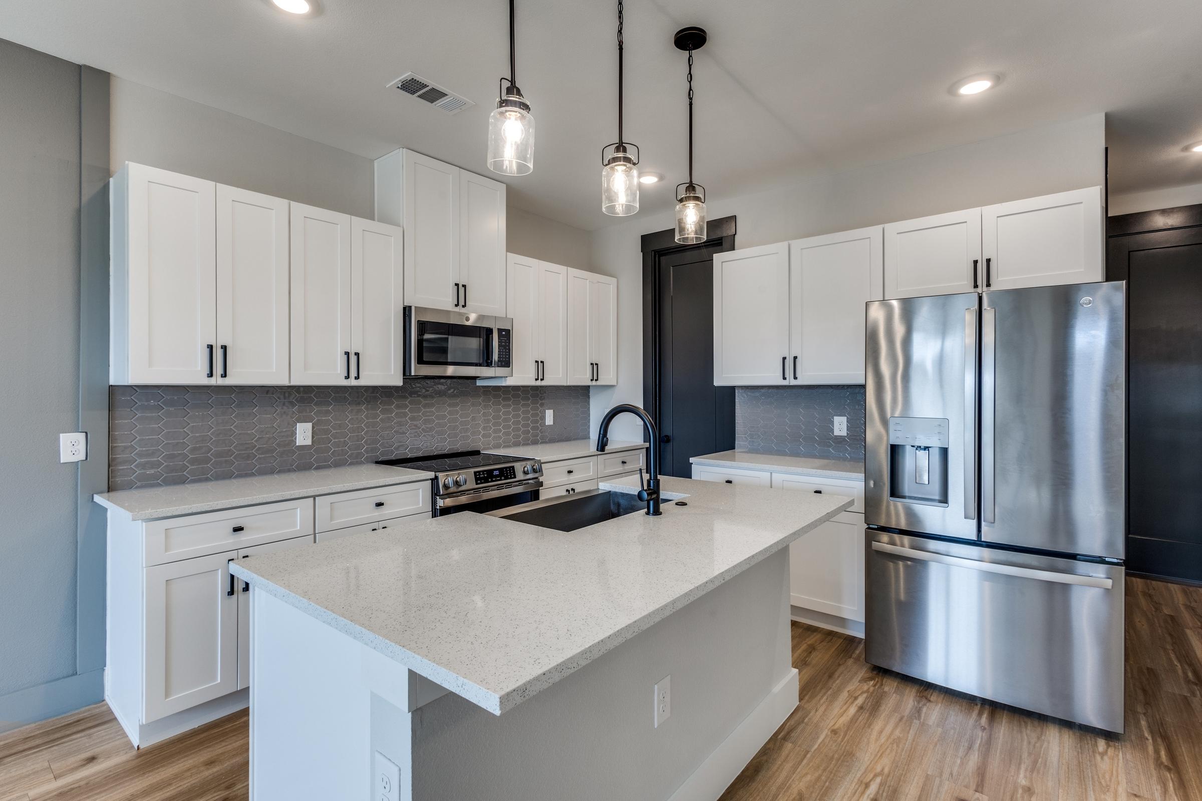 Modern apartment kitchen with white shaker cabinets, quartz island, and pendant lighting in Princeton, Texas