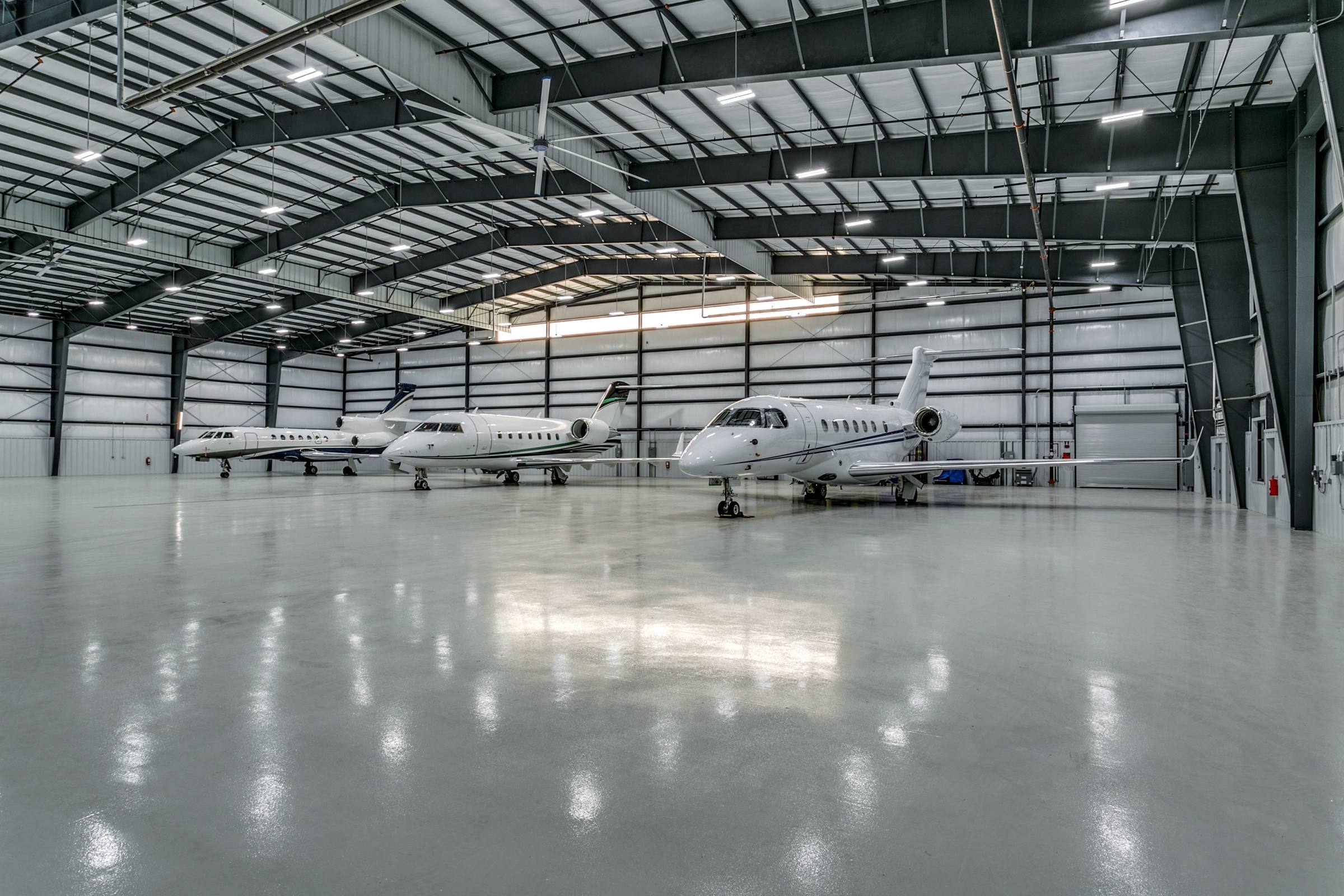 Private jet hangar interior with three business jets on polished concrete floor under steel truss ceiling in Fort Worth, Texas