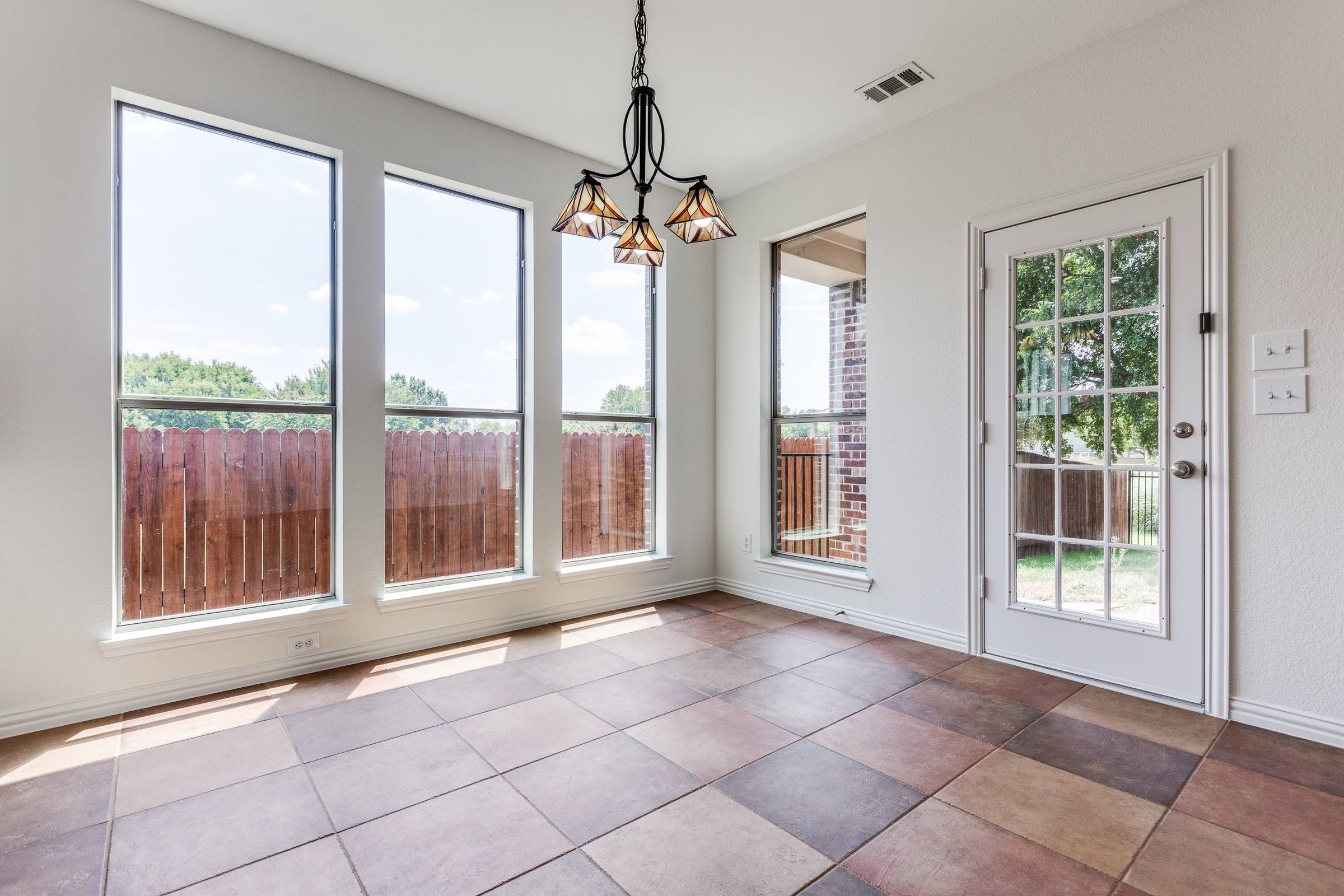 Empty dining area with Tiffany-style chandelier, large windows, french door, and tile floors before virtual staging in McKinney, Texas