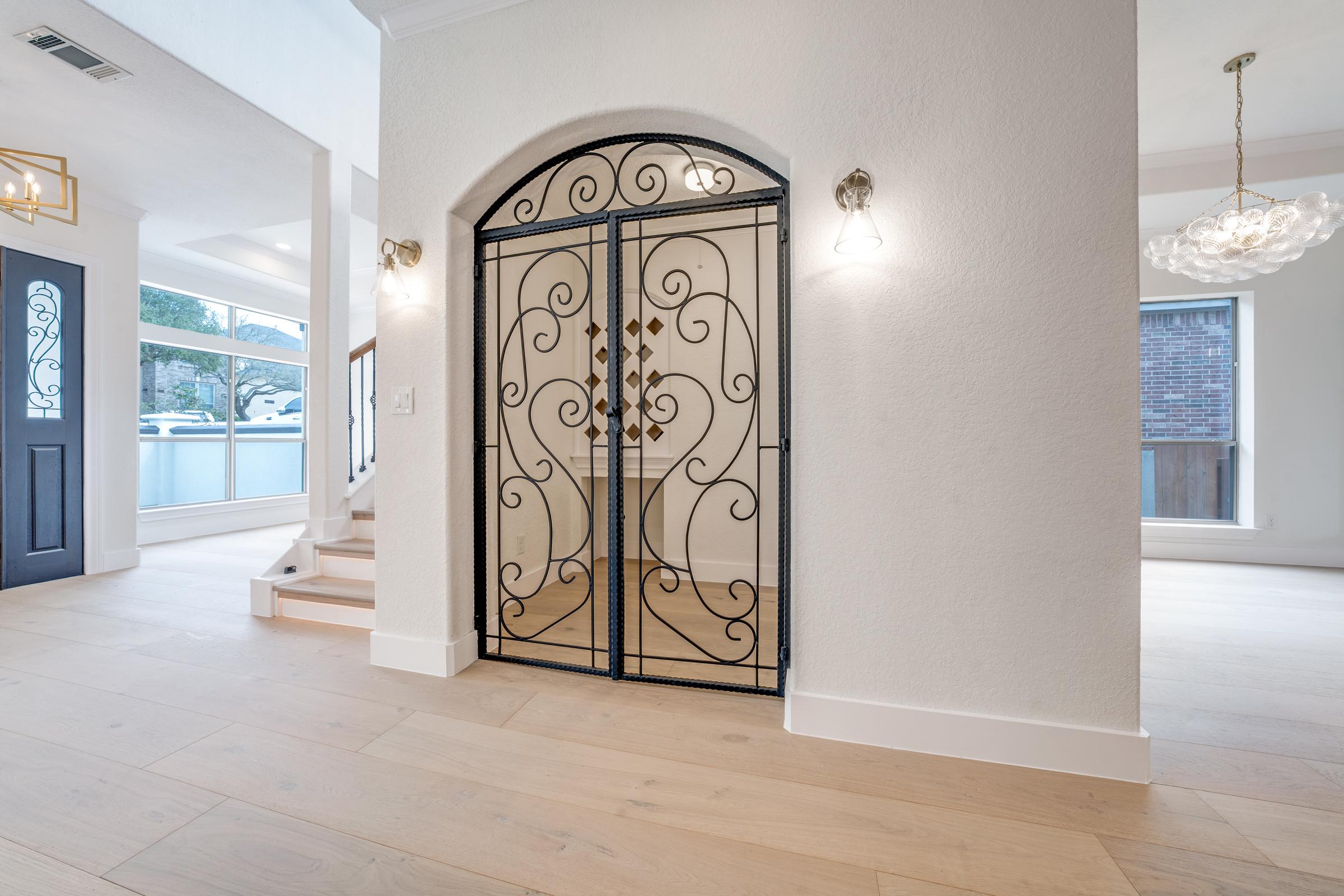 Arched wrought-iron gate leading to a wine room in the entry of a San Antonio home with light wood floors