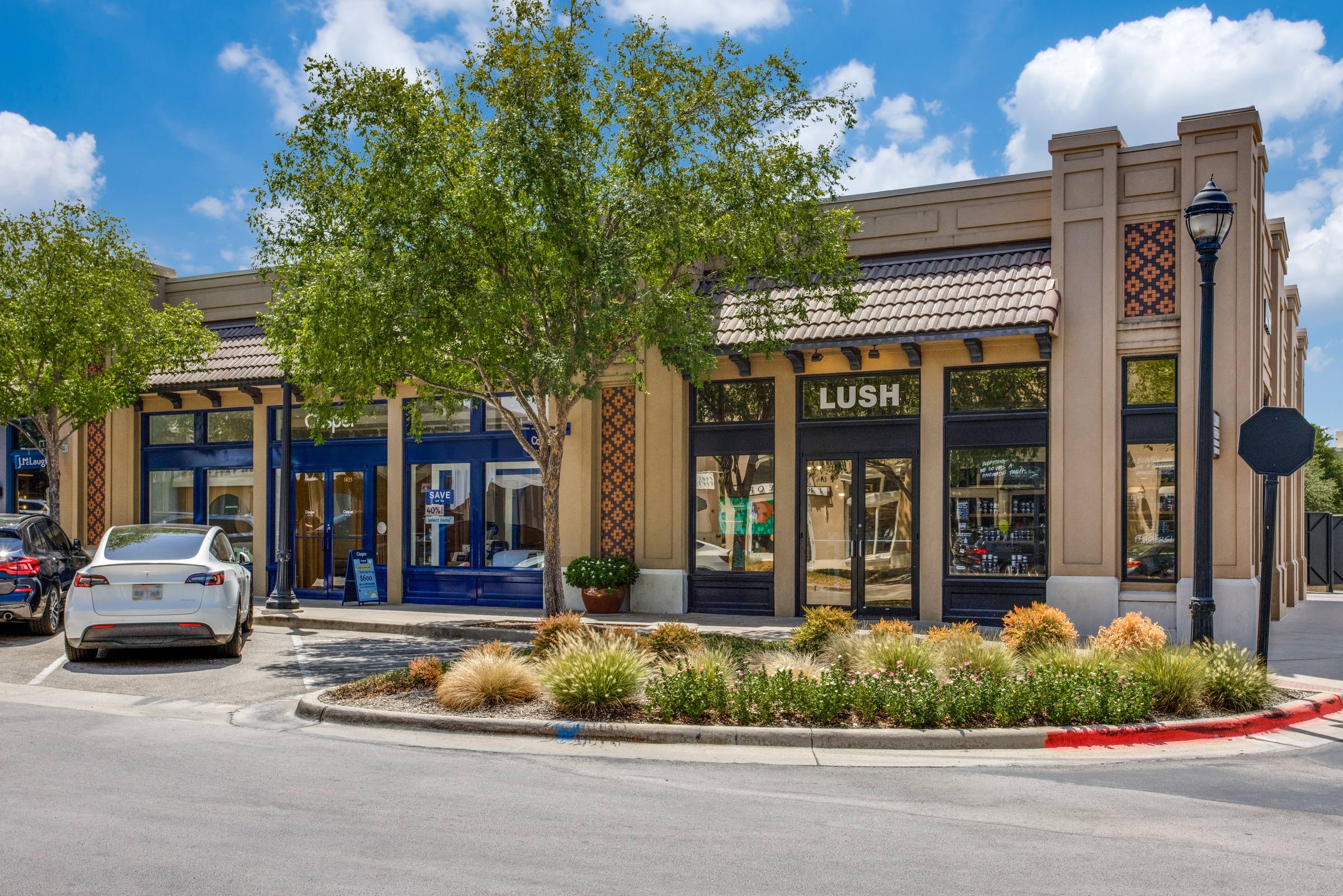 Daytime photo of a retail strip center with parked cars before digital twilight enhancement in Dallas, Texas