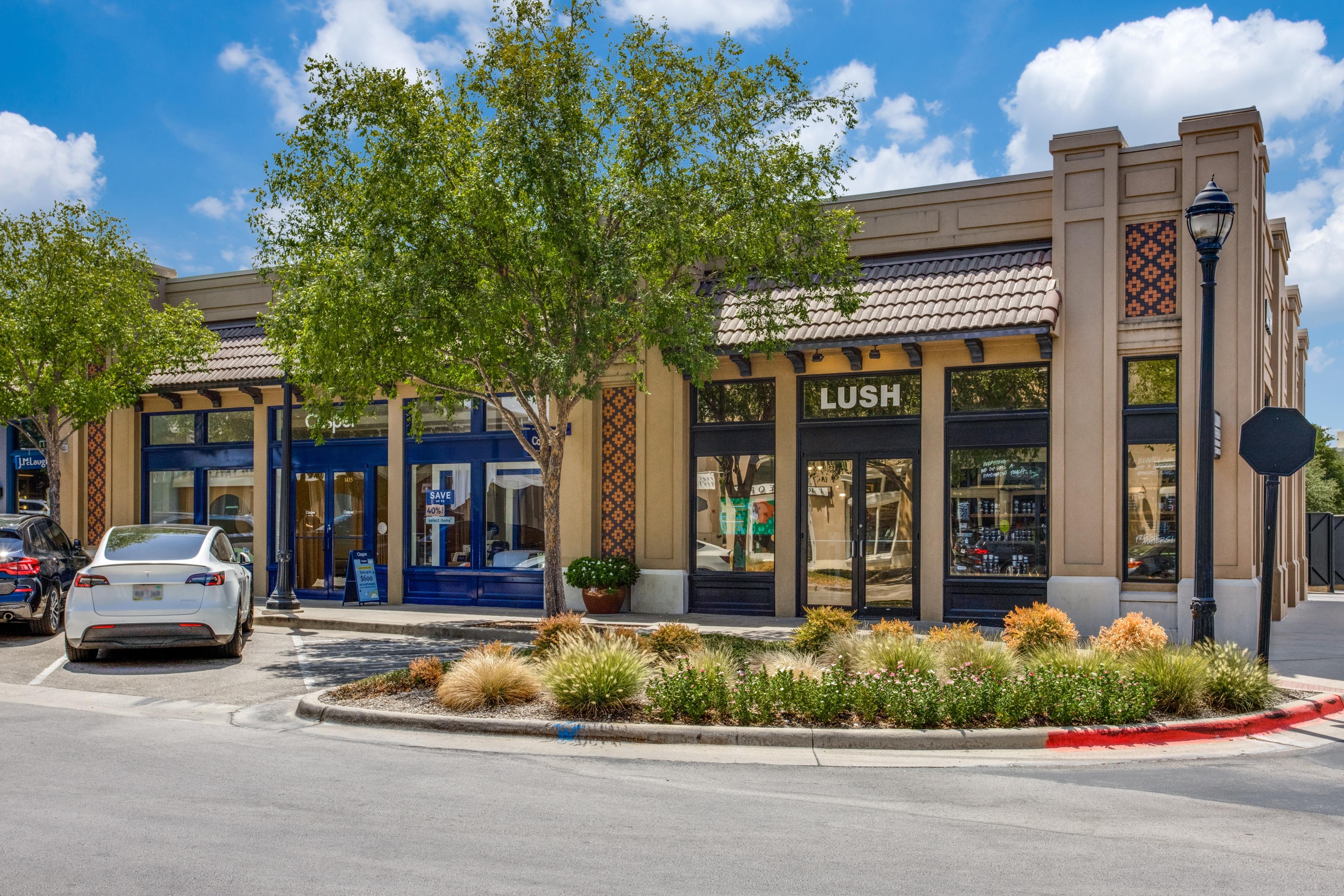 Daytime photo of a retail strip center with parked cars before digital twilight enhancement in Dallas, Texas