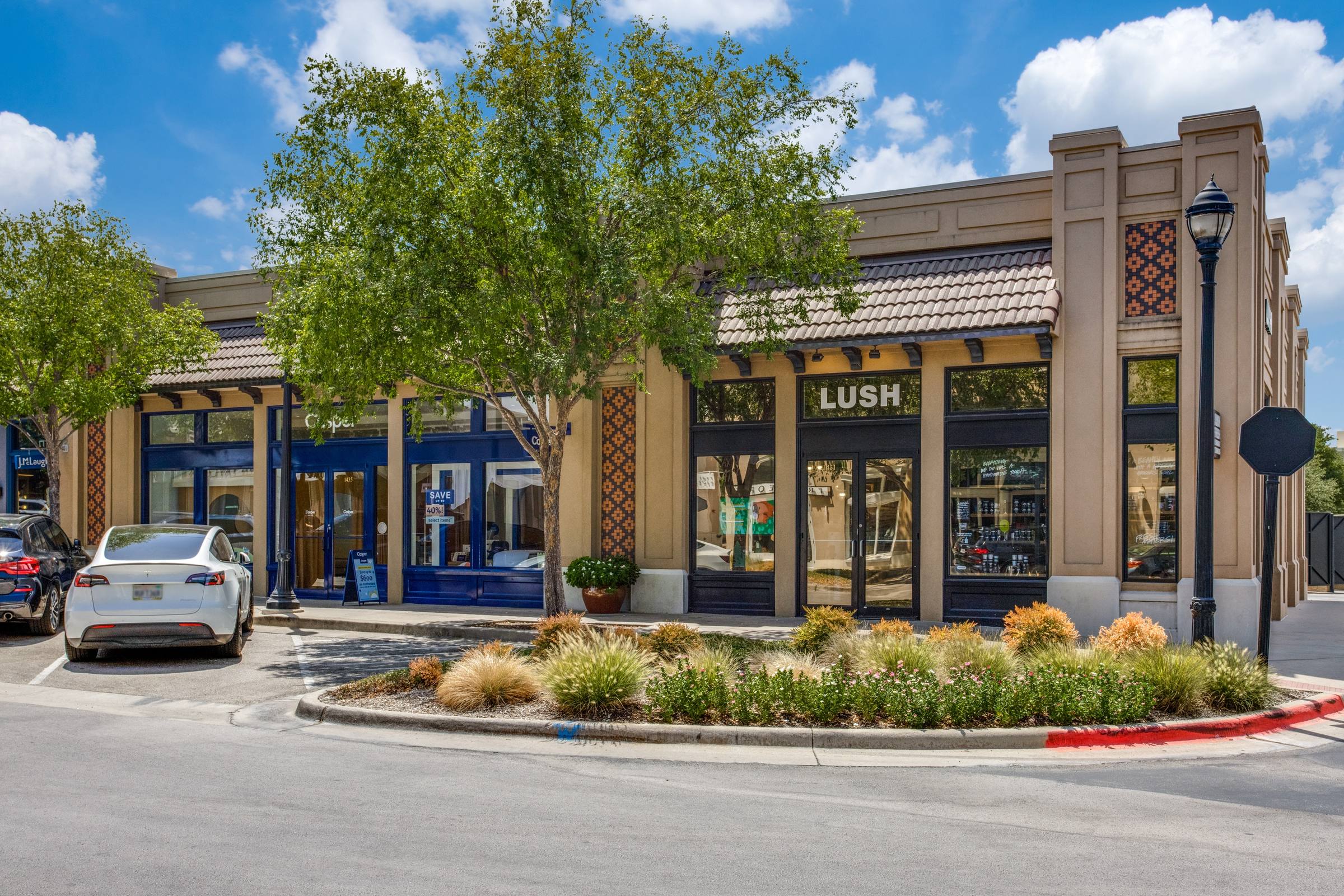 Daytime photo of a retail strip center with parked cars before digital twilight enhancement in Dallas, Texas