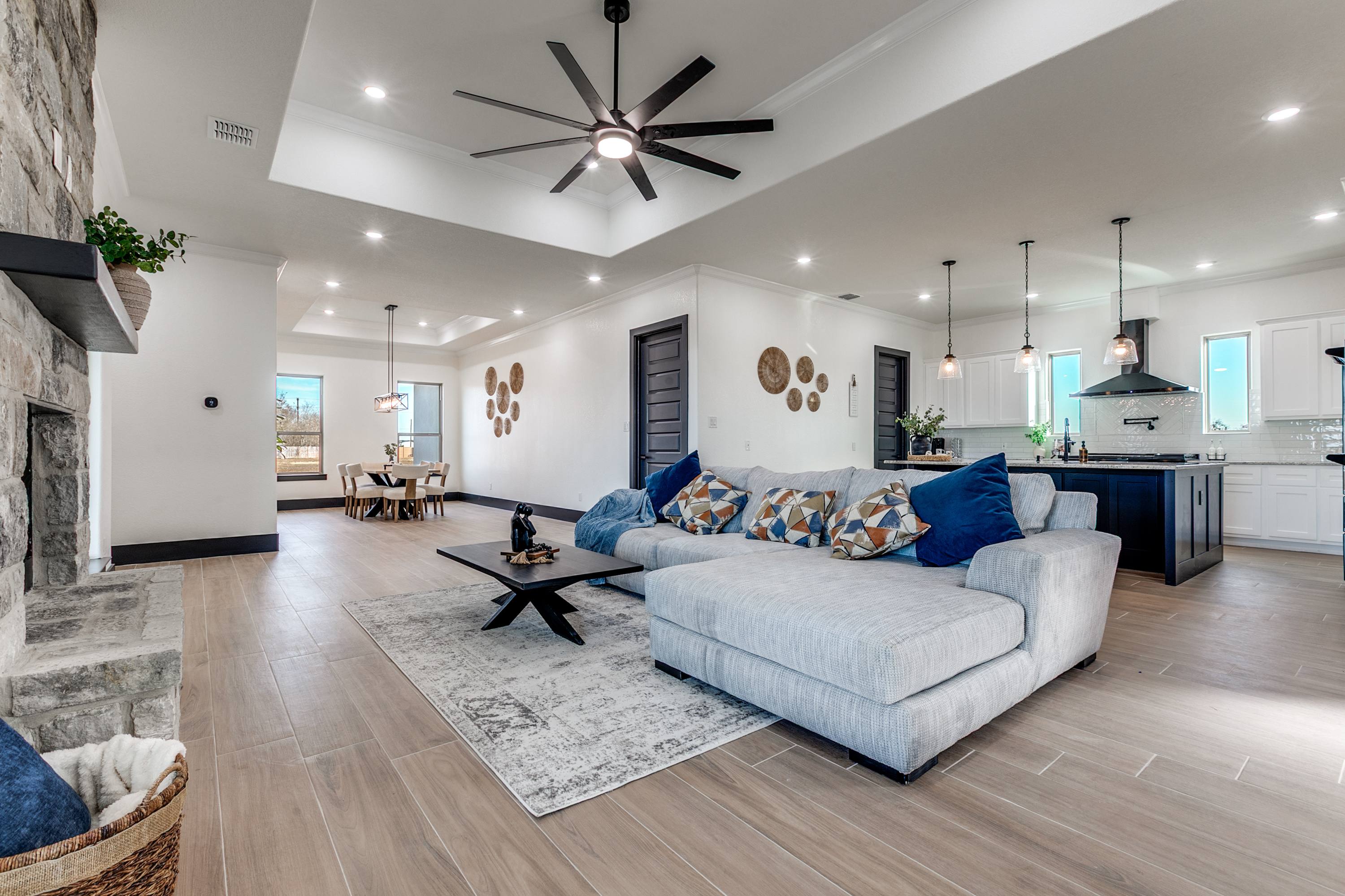 Open-concept living, dining, and kitchen area with a gray sectional and stone fireplace in a Castroville home
