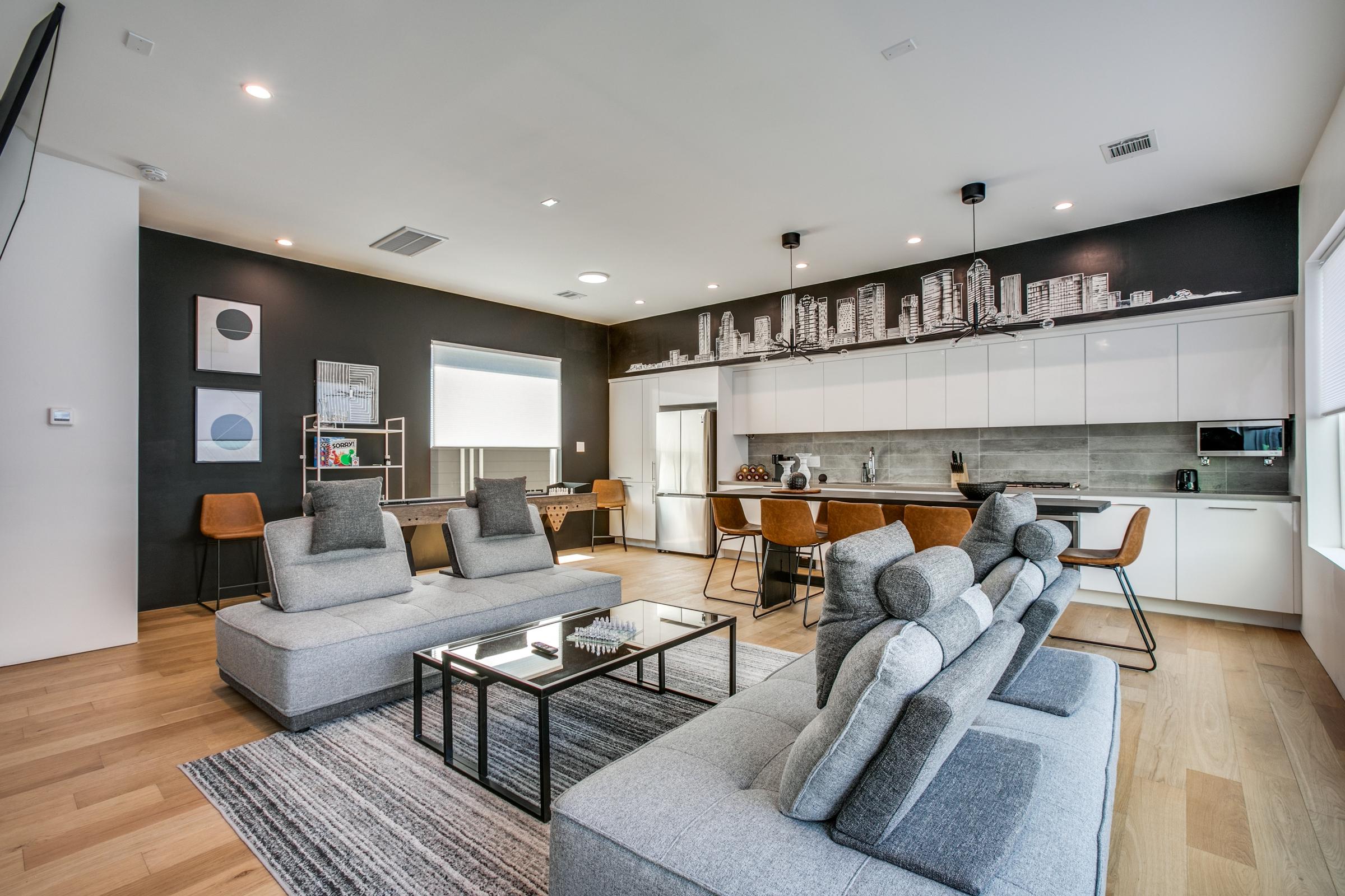 Modern open-concept great room with grey sectional sofas, cityscape mural accent wall, and kitchen bar in Houston, Texas