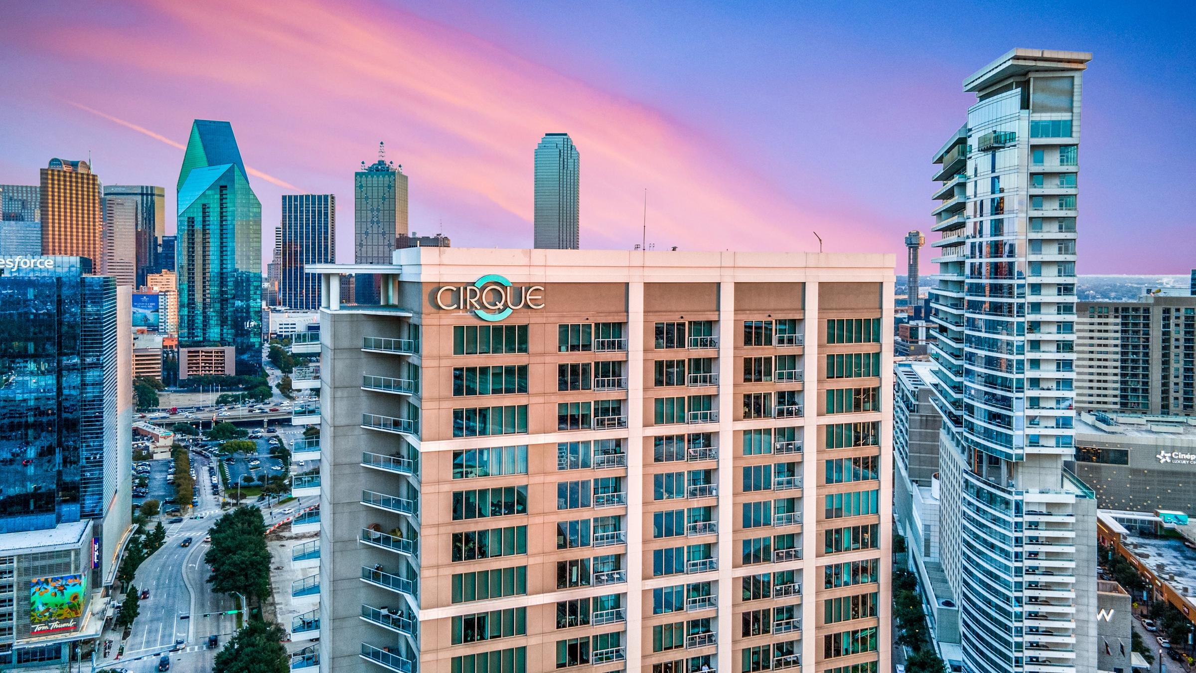 Aerial drone photograph of the Cirque high-rise apartment building at twilight with the Downtown Dallas skyline in the background in Dallas, Texas