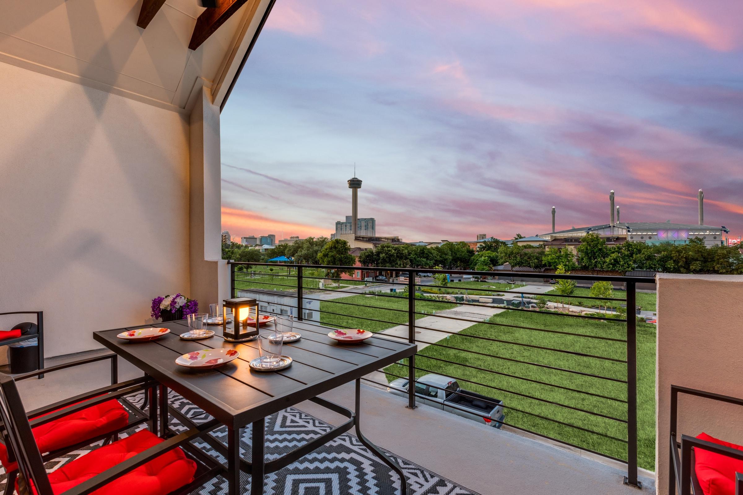 Vacation rental rooftop balcony with candlelit dining table and panoramic view of the Tower of the Americas and San Antonio skyline at twilight