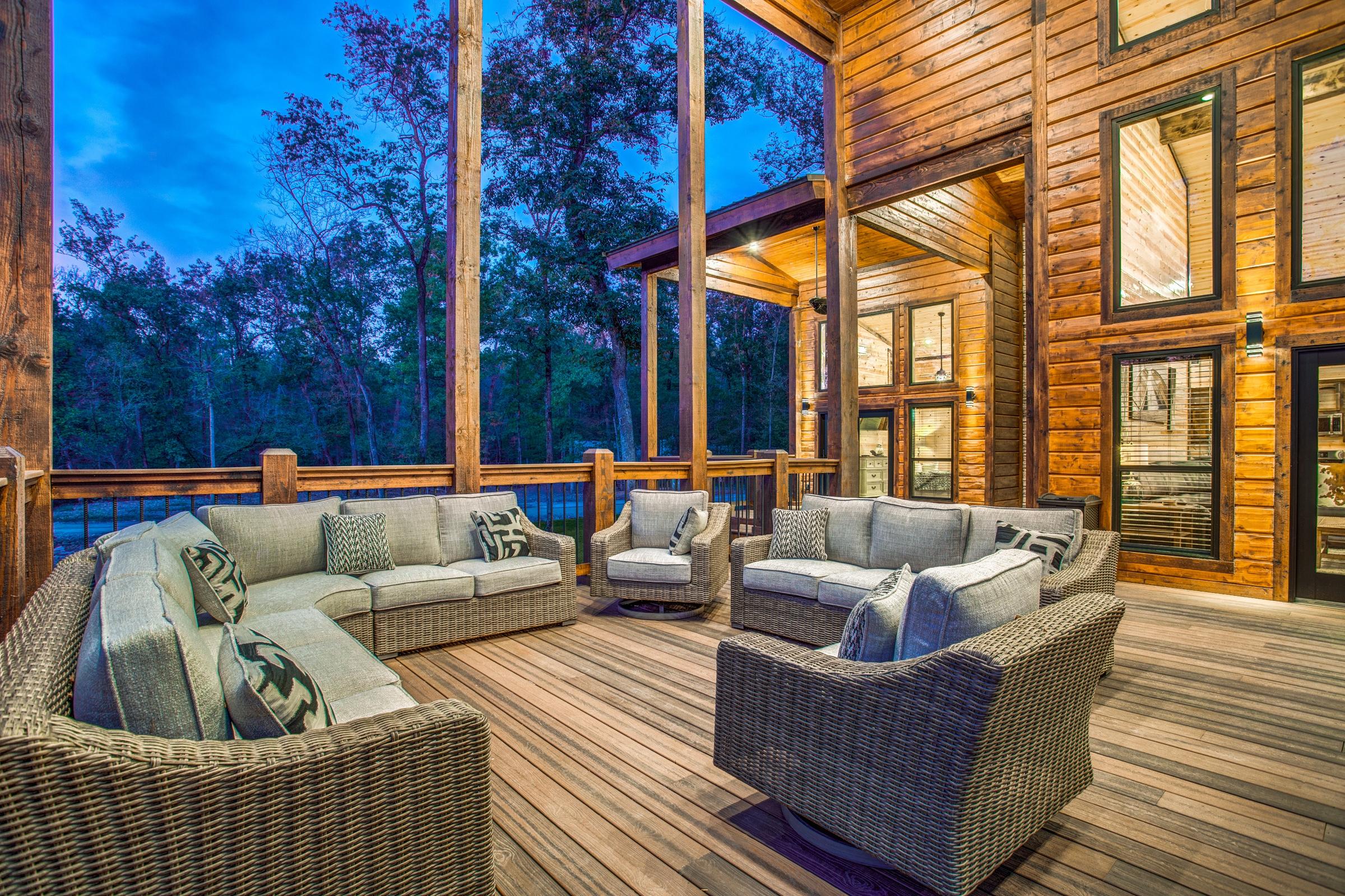 Log cabin covered deck with wicker furniture at twilight surrounded by forest in Broken Bow, Oklahoma