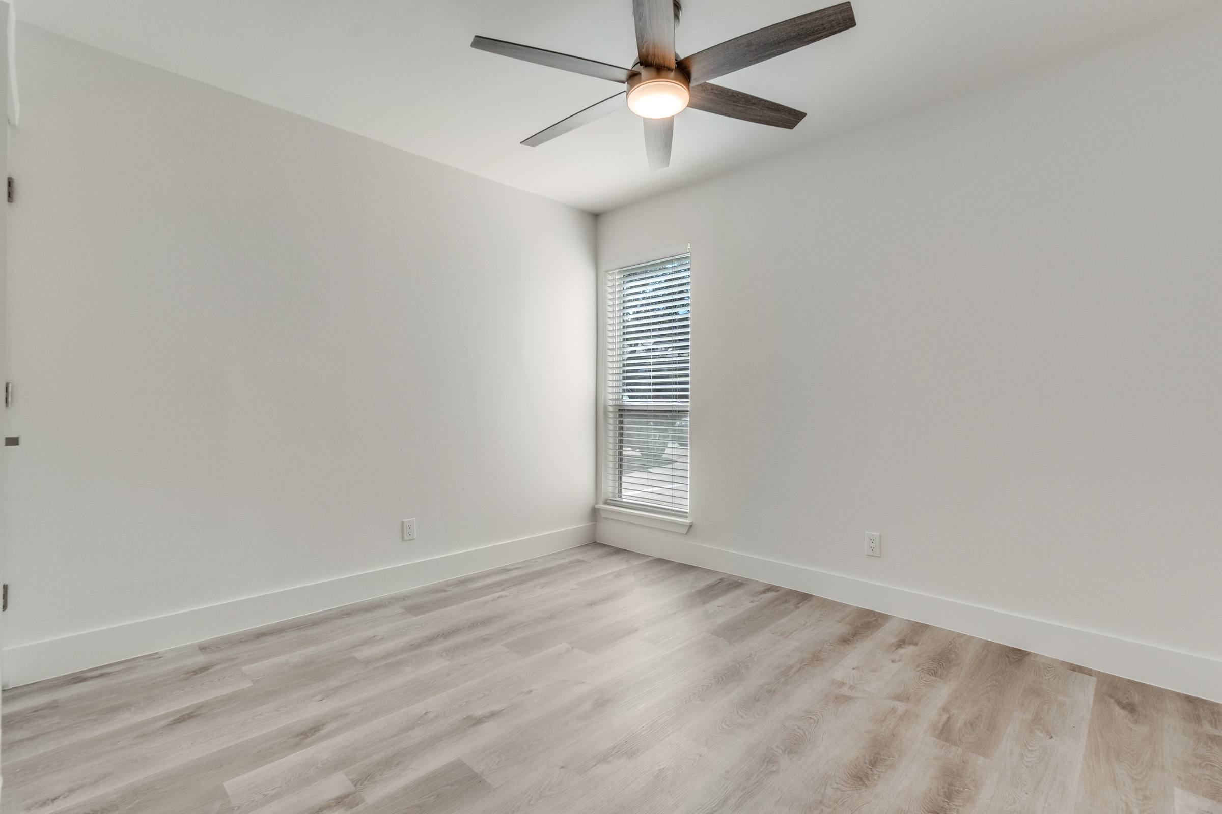Empty apartment bedroom with ceiling fan and light wood flooring before virtual staging in Dallas, Texas