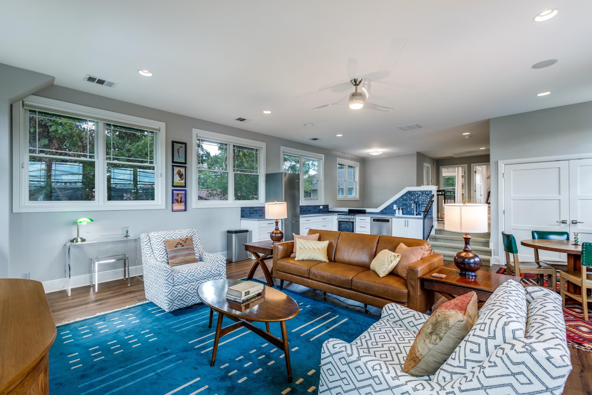 Eclectic furnished rental living room with leather sofa, blue area rug, and open kitchen in Austin, Texas