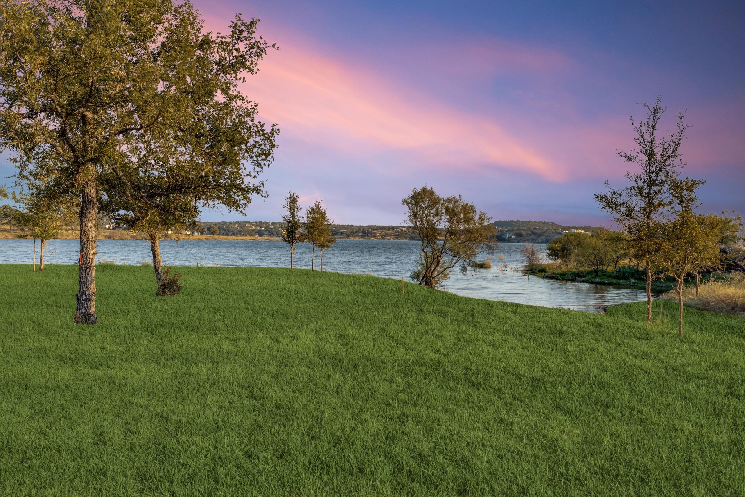 Lush green lakefront lawn with scattered trees and pink-purple twilight sky overlooking a Texas Hill Country lake in Burnet, Texas