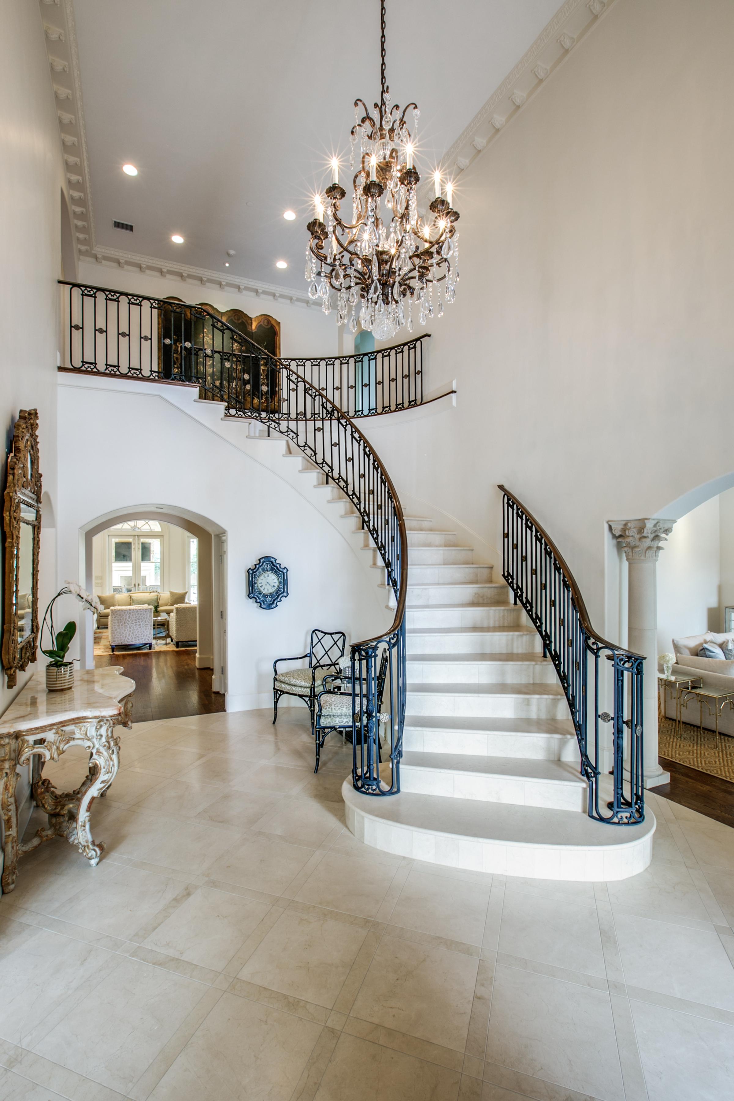Two-story Southlake, TX entryway featuring a crystal chandelier, curved white staircase with black iron balusters, carved gold console table, and marble tile floor.