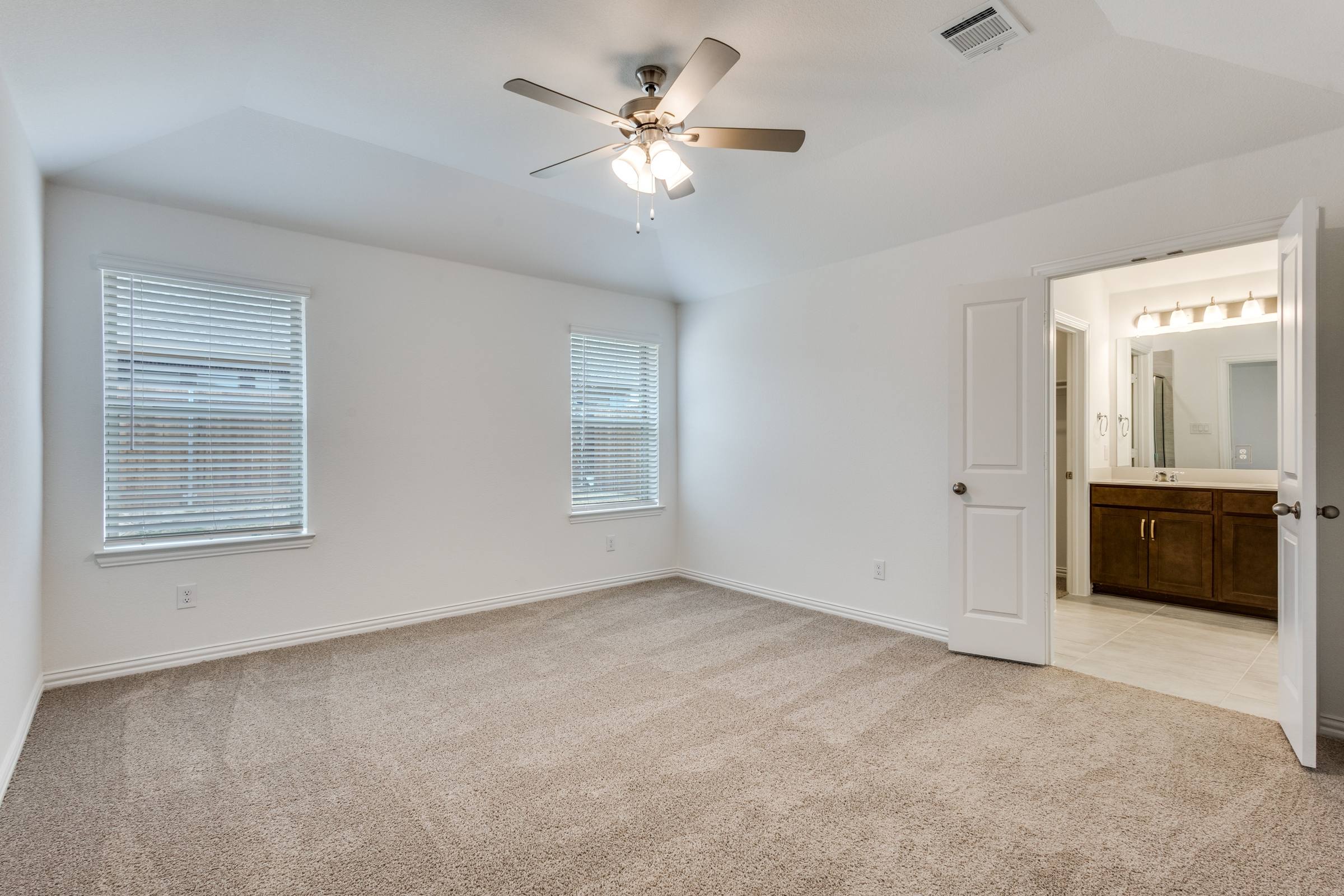 Vacant master bedroom with en-suite bathroom, carpet, and ceiling fan in Anna, Texas before virtual staging