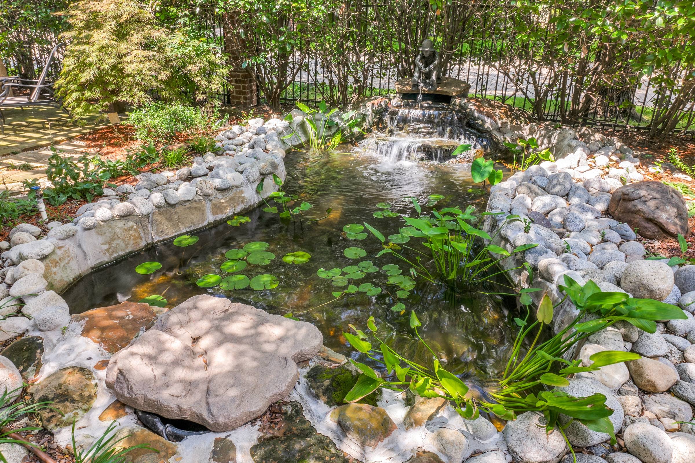 Backyard koi pond with stacked-stone waterfall, river rock borders, and lush landscaping in Richardson, Texas.