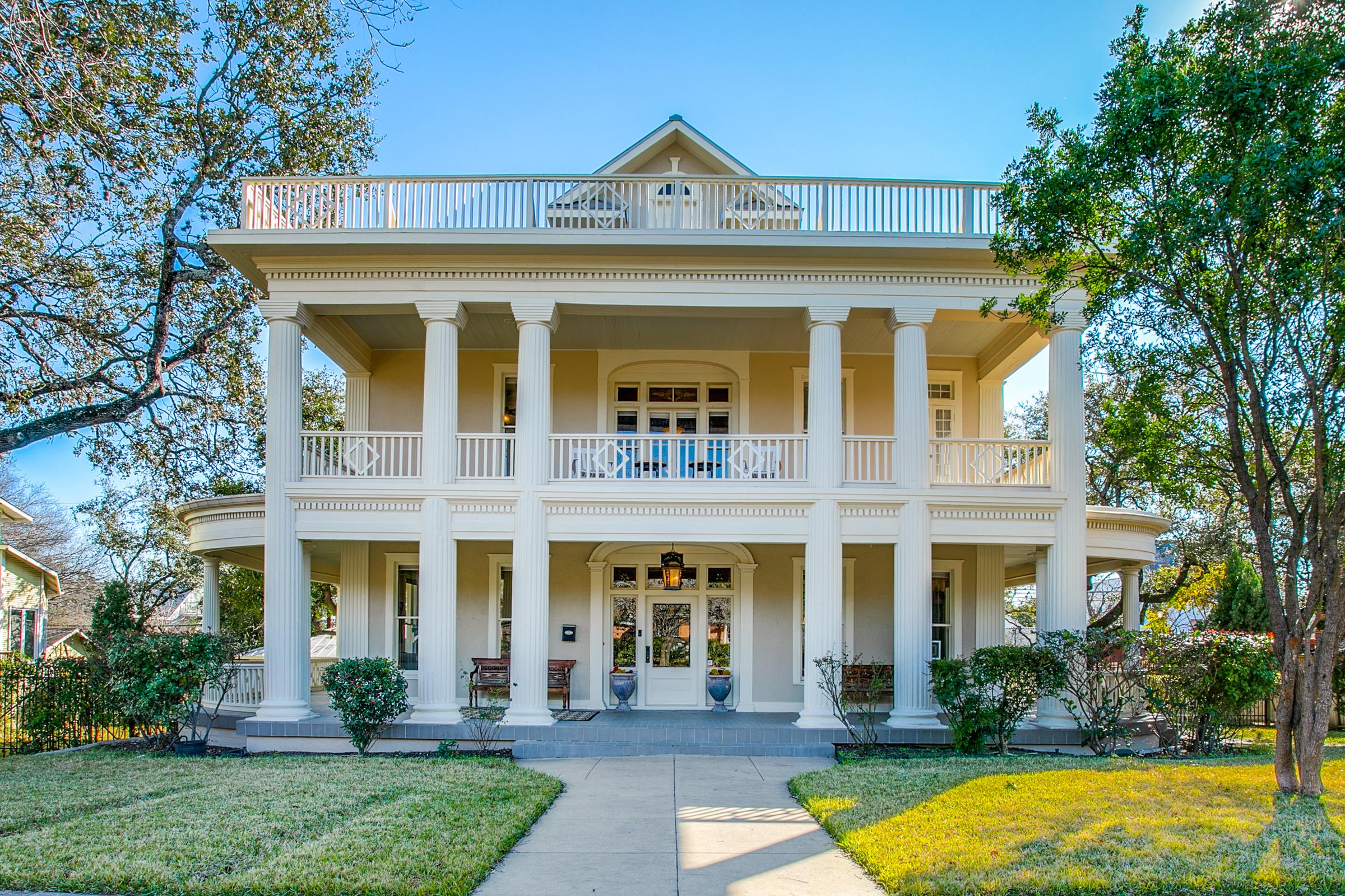 Grand two-story home with white columns and double front porches framed by oak trees in San Antonio