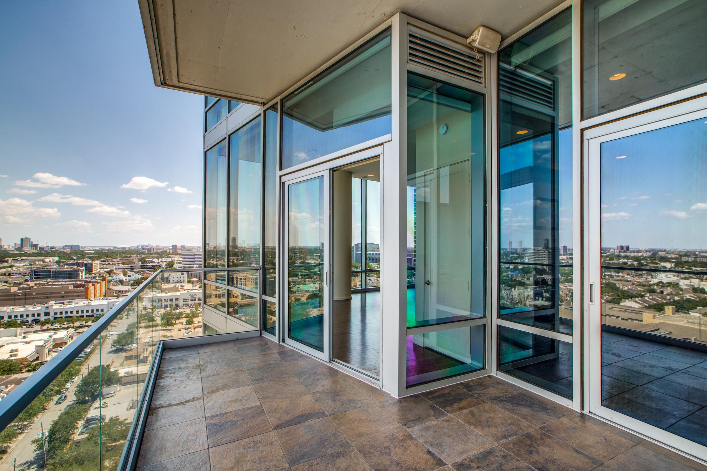 Private high-rise condo terrace with tile flooring, glass railing, and floor-to-ceiling windows overlooking Houston