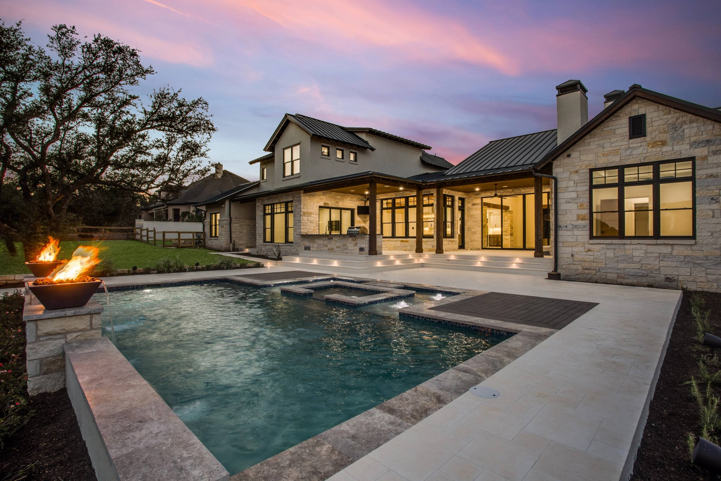 Backyard pool with fire bowls and a new-build Hill Country home at twilight in Austin, TX
