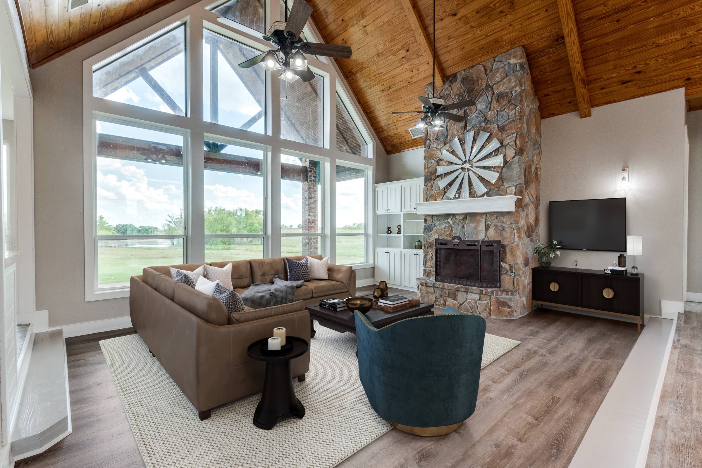 Virtually staged living room with sectional sofa, accent chair, TV console, and area rug beneath vaulted wood ceiling and stone fireplace in Ennis, Texas