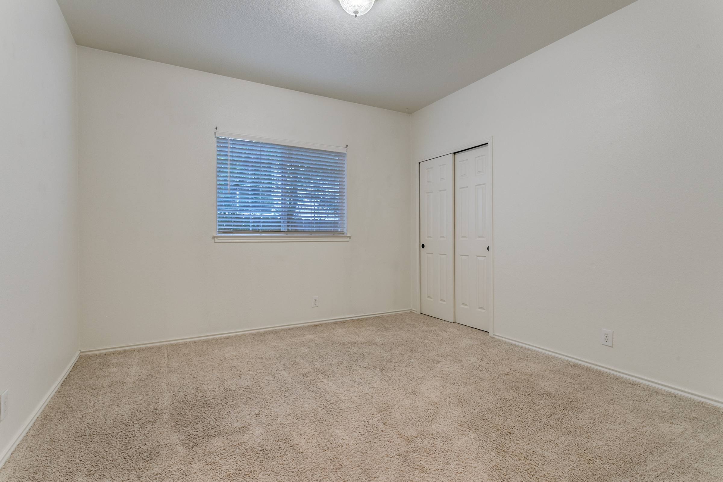 Vacant living room with window blinds, carpet, and closet door in a San Antonio, Texas rental property before virtual staging