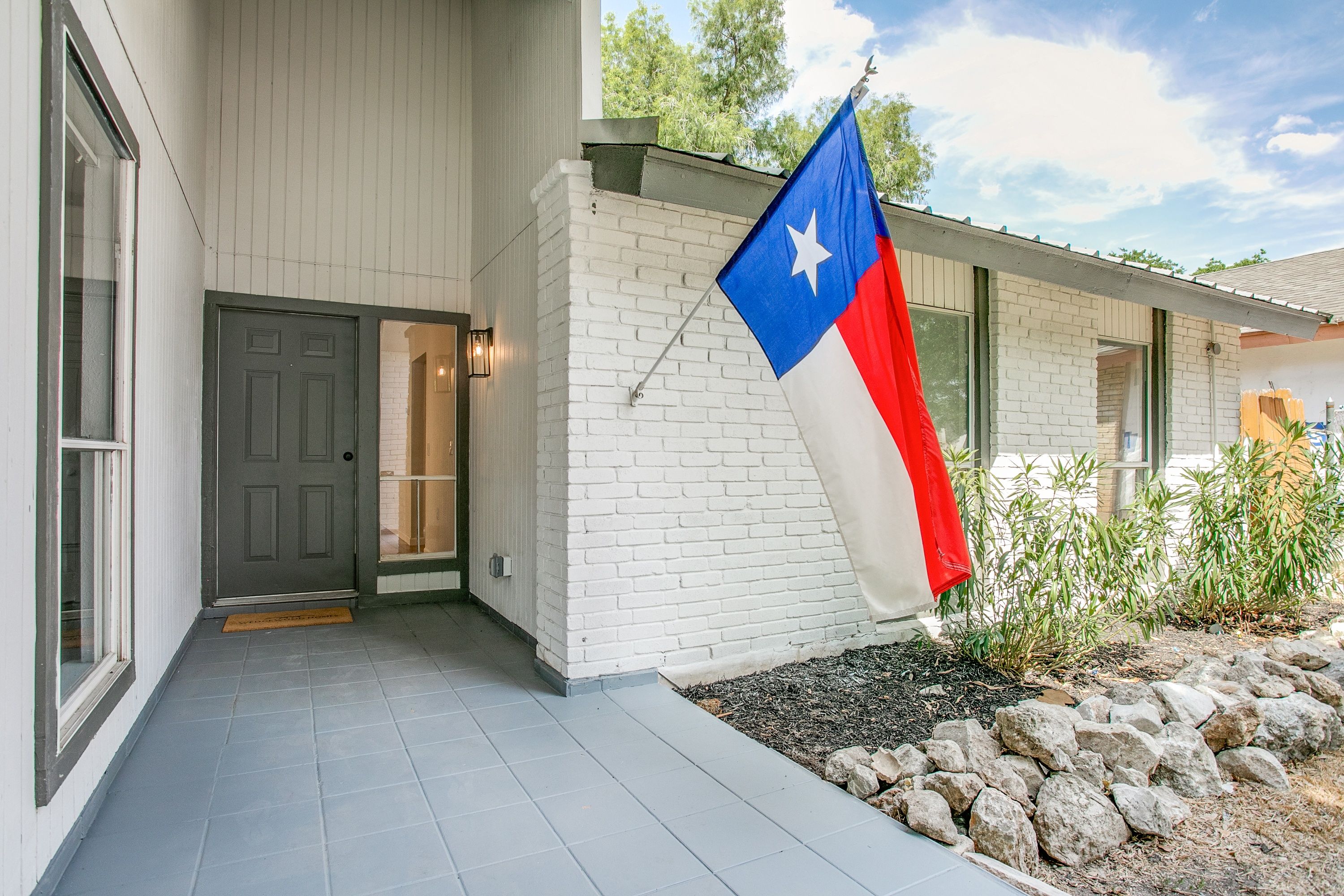 Front porch of a mid-century modern white brick home with a Texas flag in San Antonio, Texas