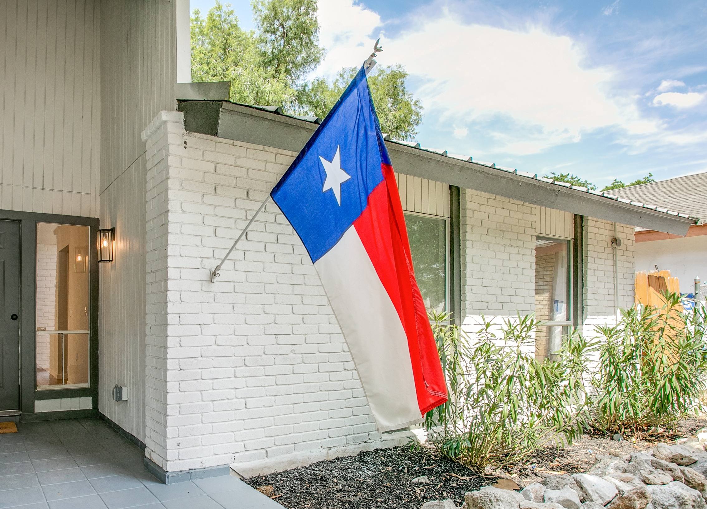 Front porch of a mid-century modern white brick home with a Texas flag in San Antonio, Texas