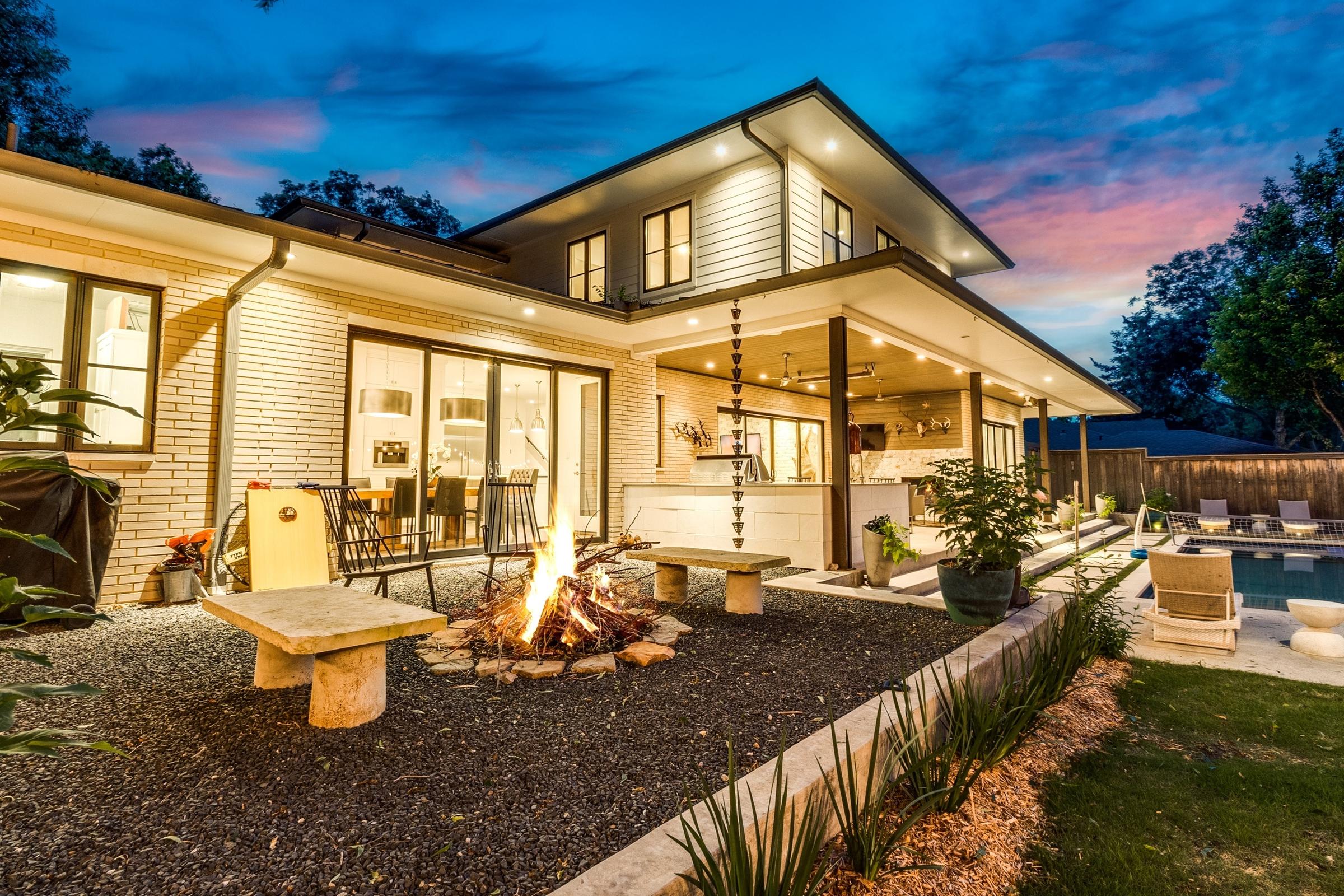 Modern two-story home with outdoor kitchen, fire pit, and pool at twilight in Dallas, Texas