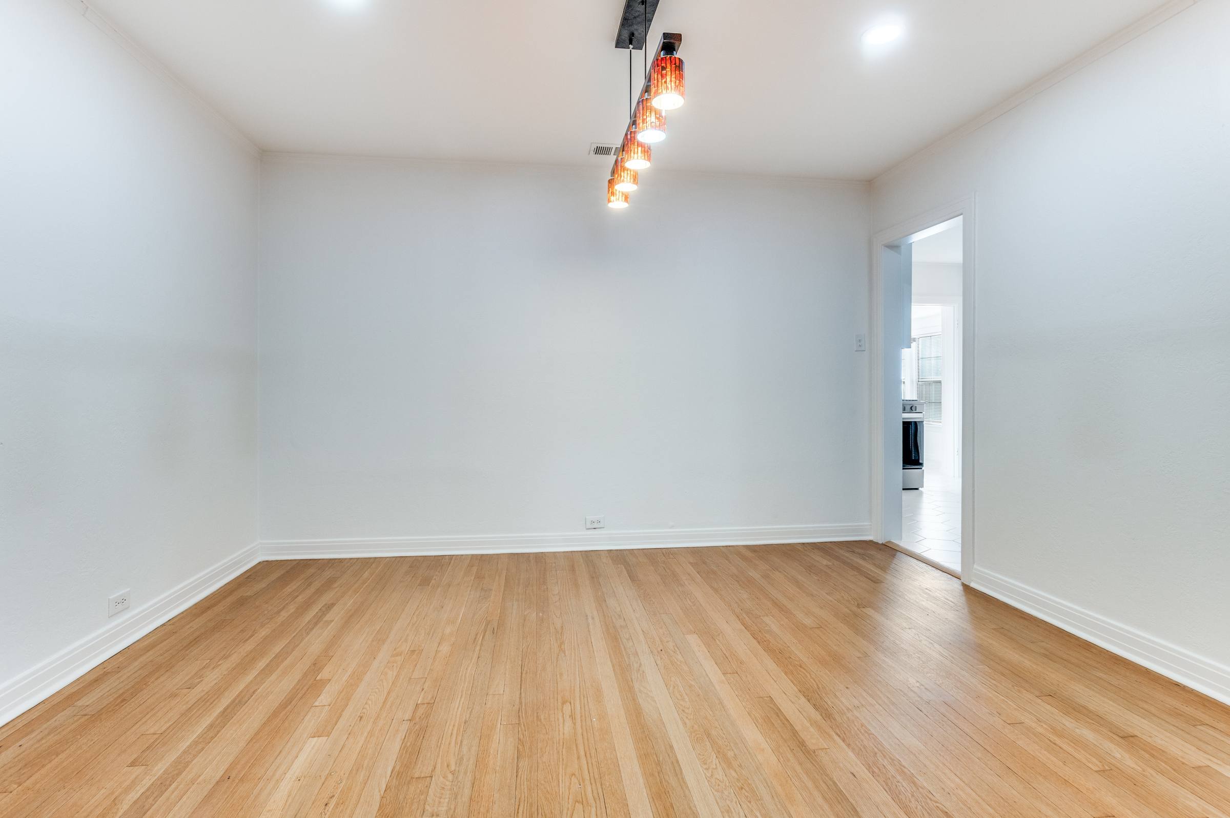 Empty apartment dining room with hardwood floors and modern pendant chandelier before virtual staging in Dallas, Texas