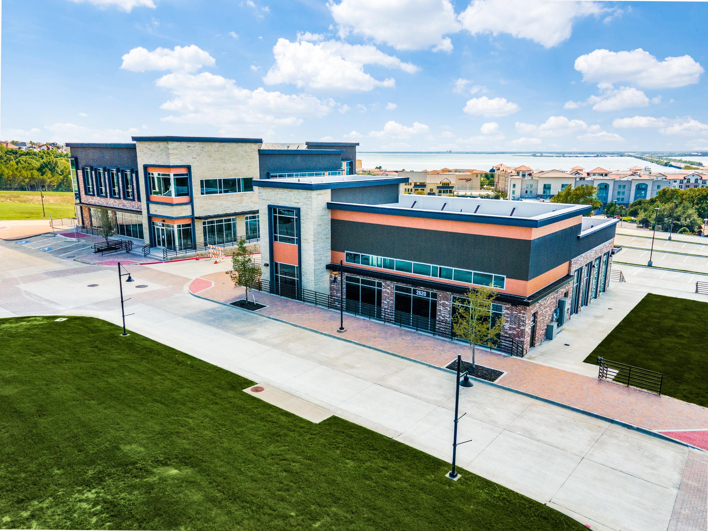 Aerial drone view of a modern commercial retail development with stone and metal facade near a lake in Rockwall, Texas