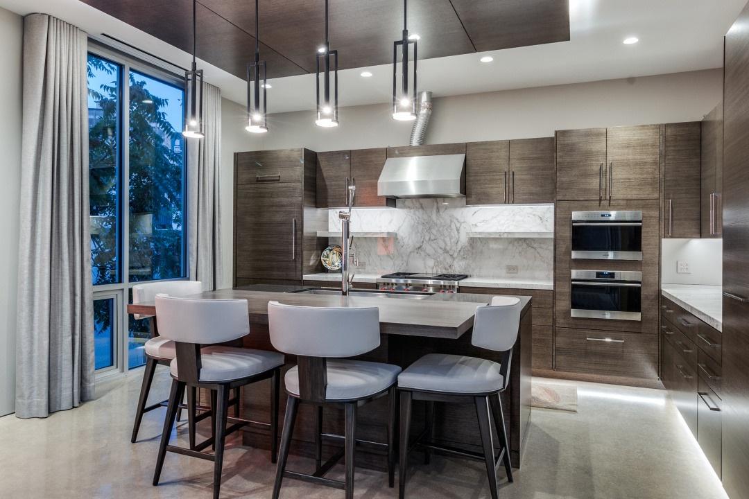 Modern luxury kitchen with dark wood cabinetry, marble backsplash, pendant lighting, and stainless steel appliances in a custom-built home in Texas