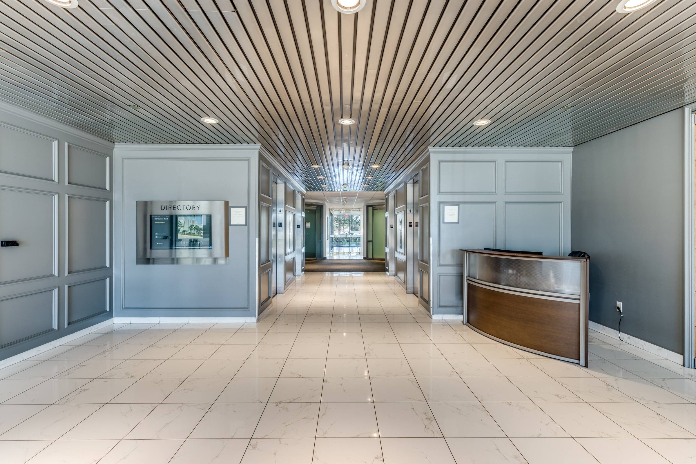 Commercial elevator lobby with slatted wood ceiling, blue wainscoted walls, directory kiosk, and reception desk in Houston, Texas.