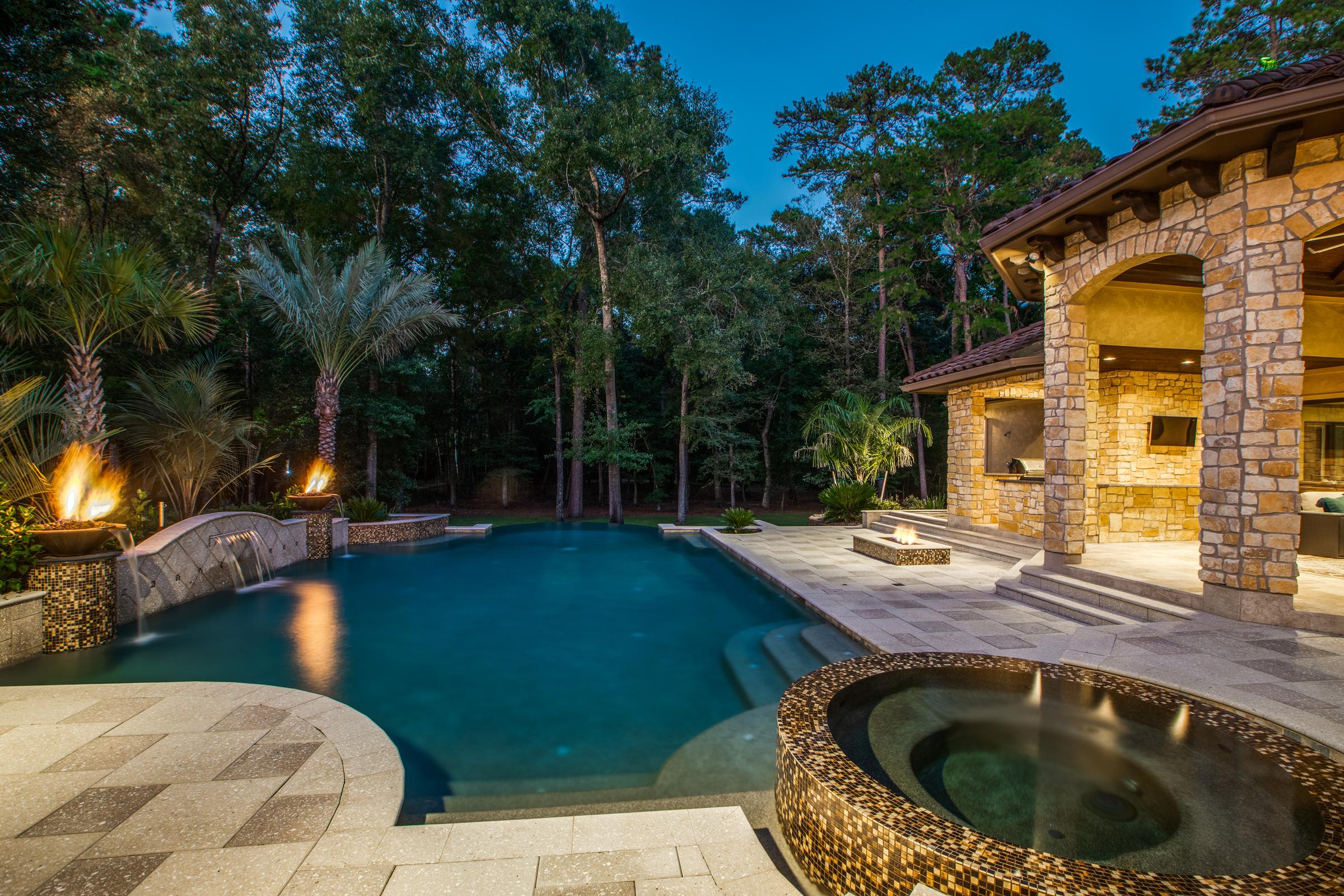 Backyard pool and spa with fire bowls, water features, and a stone loggia lit at dusk in Spring, Texas