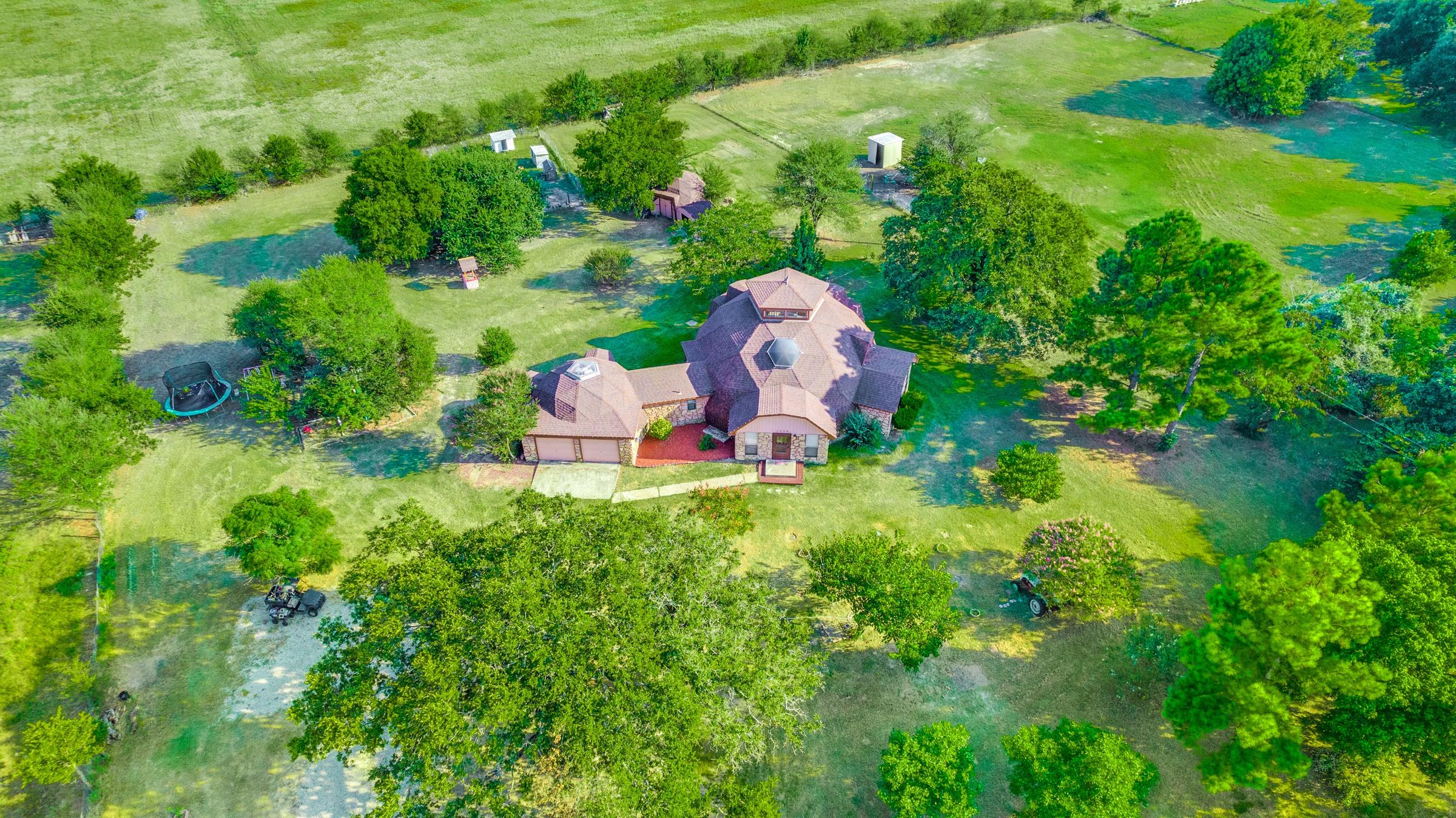 Aerial drone photograph of a geodesic dome home on a sprawling green farm property with mature trees and outbuildings in Seagoville, Texas
