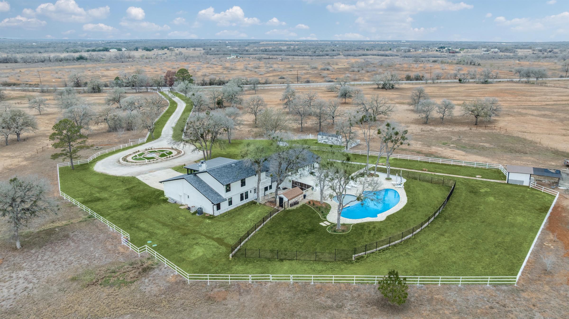 Aerial drone view of a ranch estate with pool, white fencing, circular driveway, and sprawling acreage in Lockhart, Texas