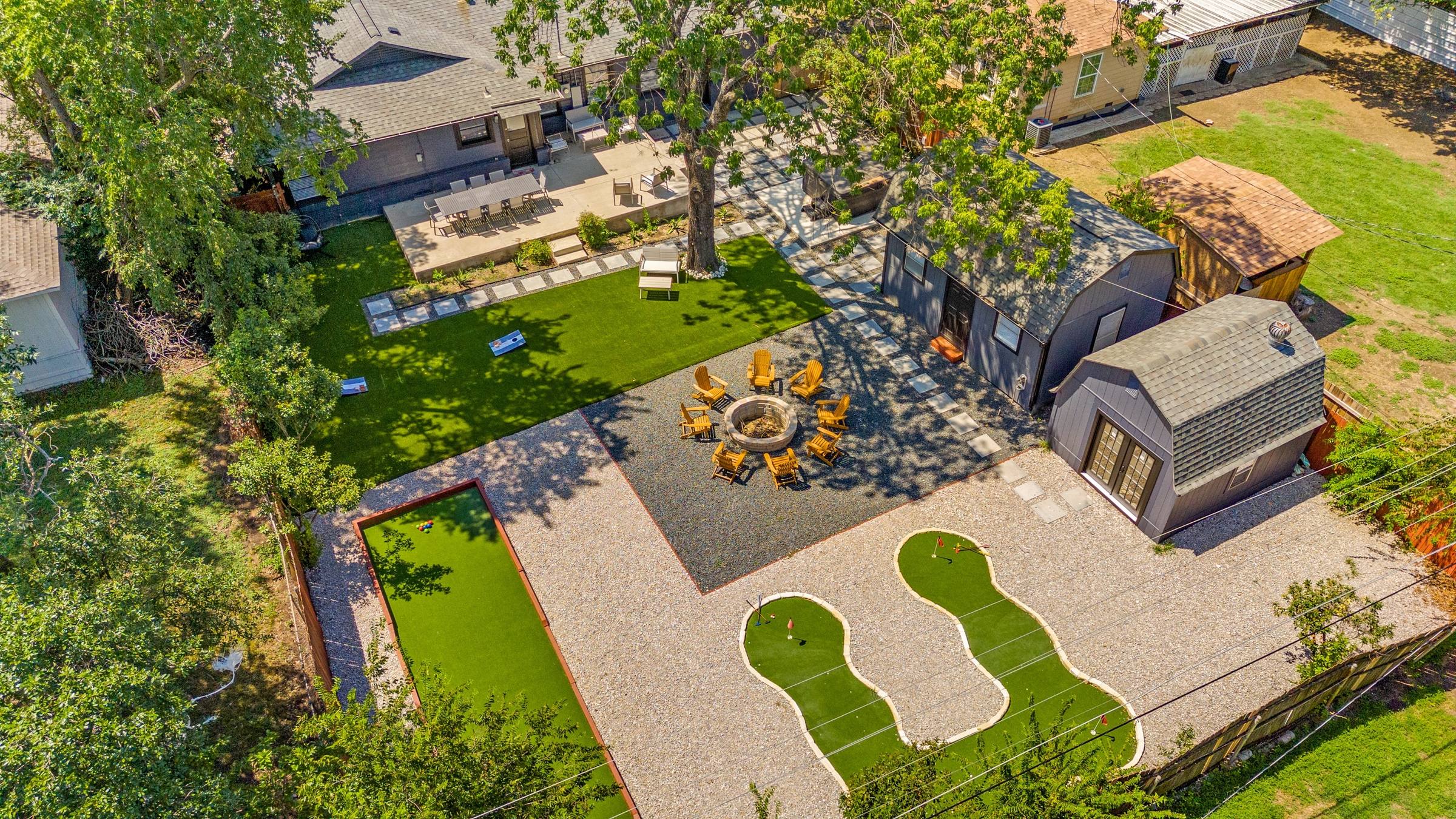 Aerial drone view of a backyard with putting green, fire pit seating area, turf lawn, and guest house in Arlington, Texas