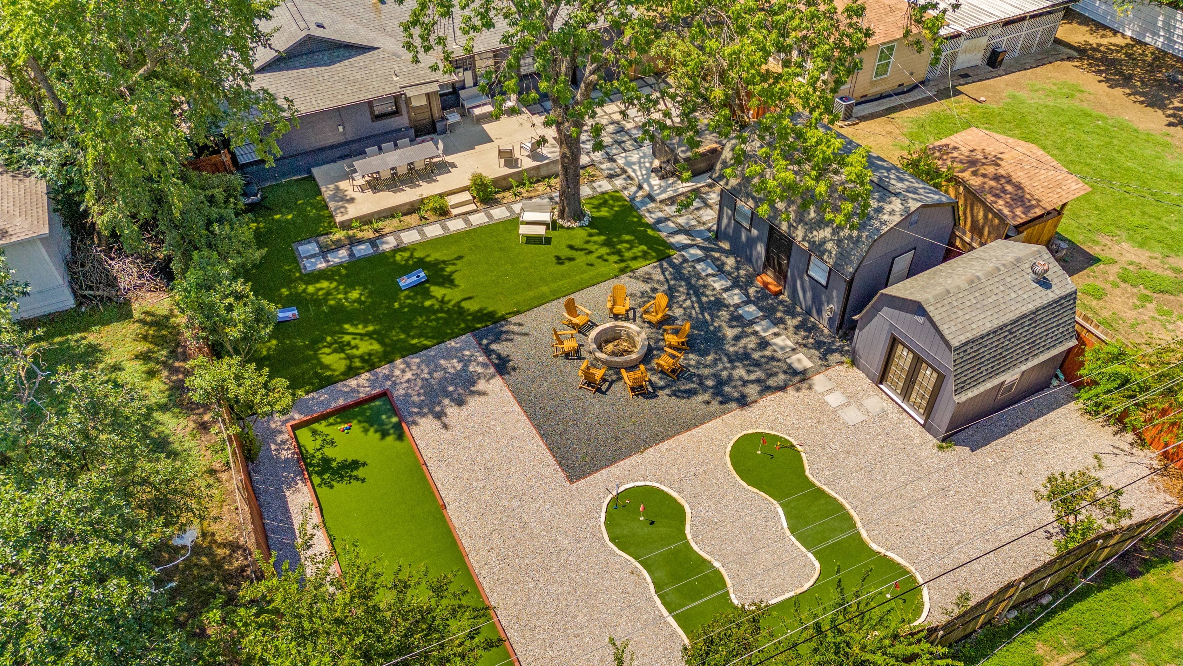 Aerial drone view of a backyard with putting green, fire pit seating area, turf lawn, and guest house in Arlington, Texas