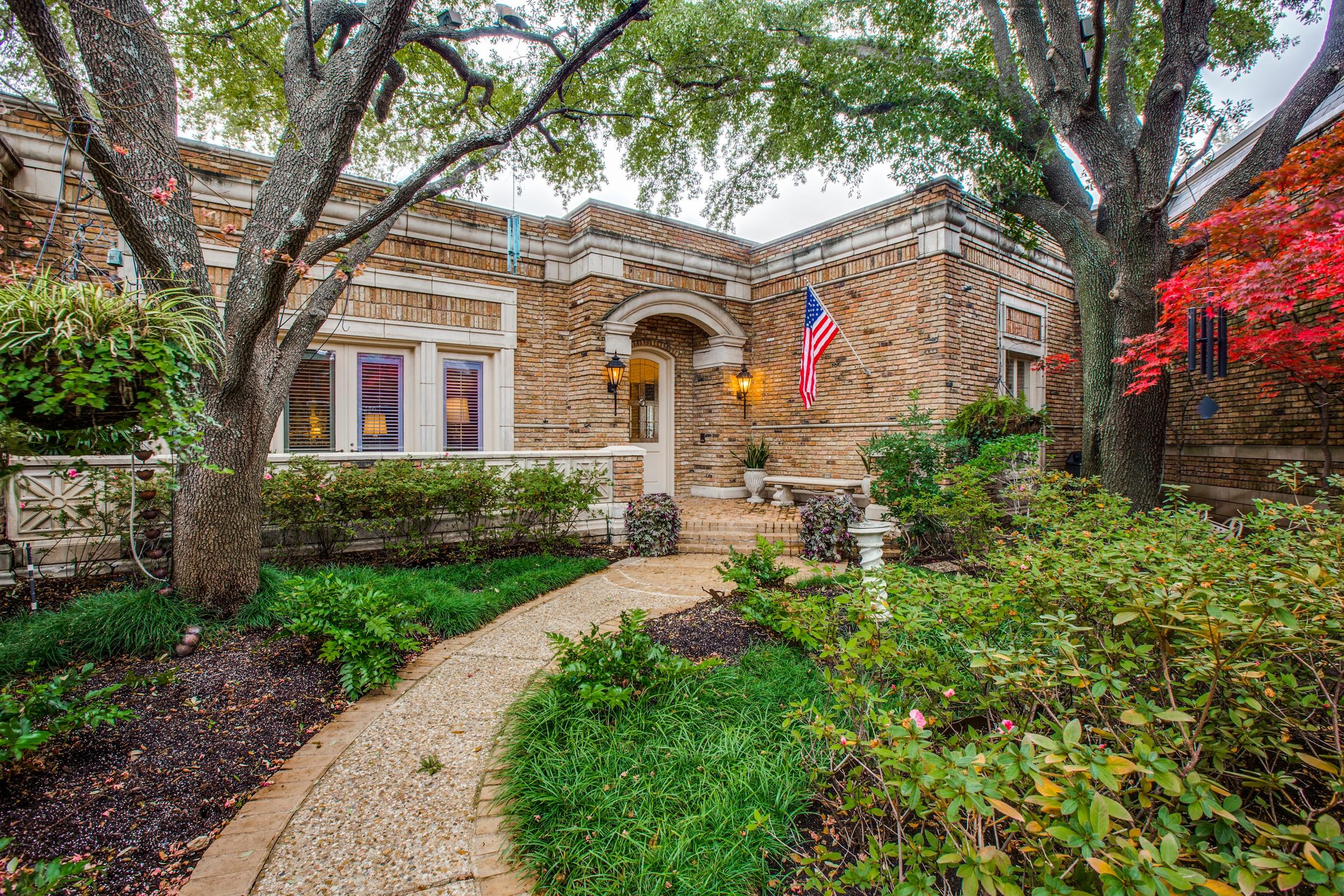 Historic brick estate with stone walkway, American flag, red Japanese maple, and mature landscaping in Dallas, Texas