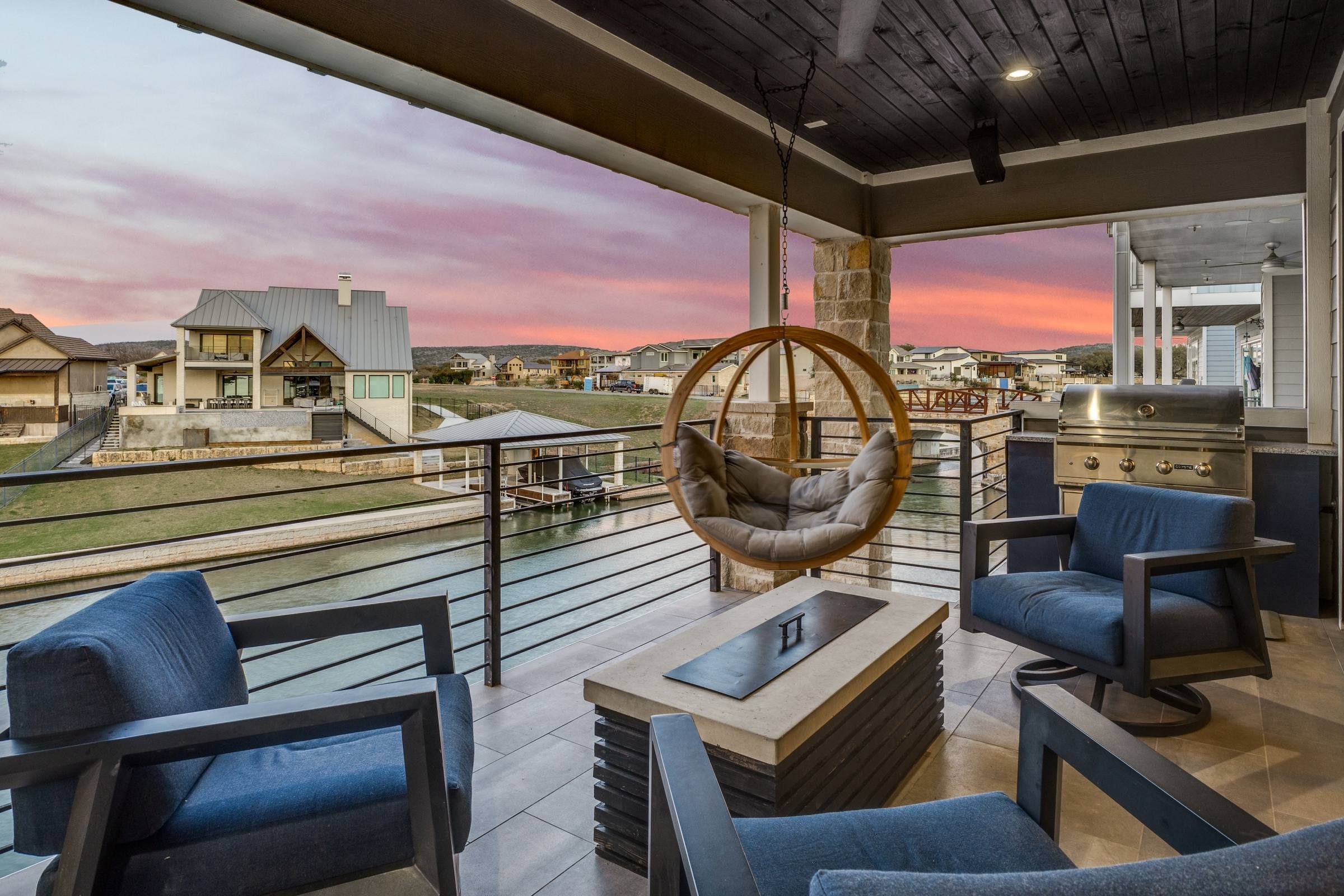 Covered patio with hanging egg chair, outdoor grill, and canal-view seating area at twilight in Kingsland, Texas
