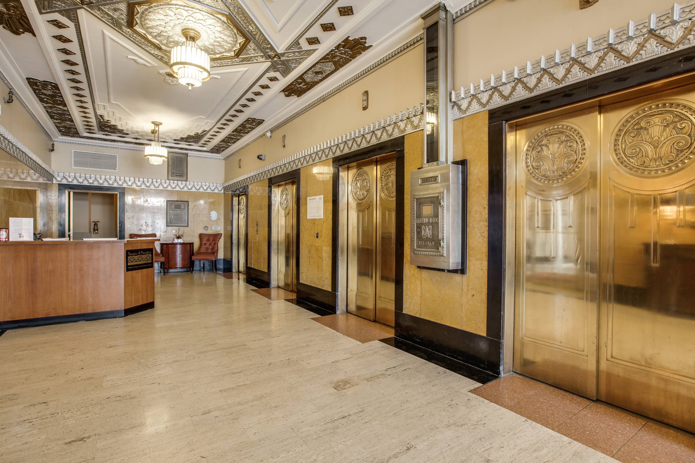 Historic art deco lobby with ornate ceiling, gold-paneled elevator doors, and marble floor in a commercial building in Fort Worth, Texas.