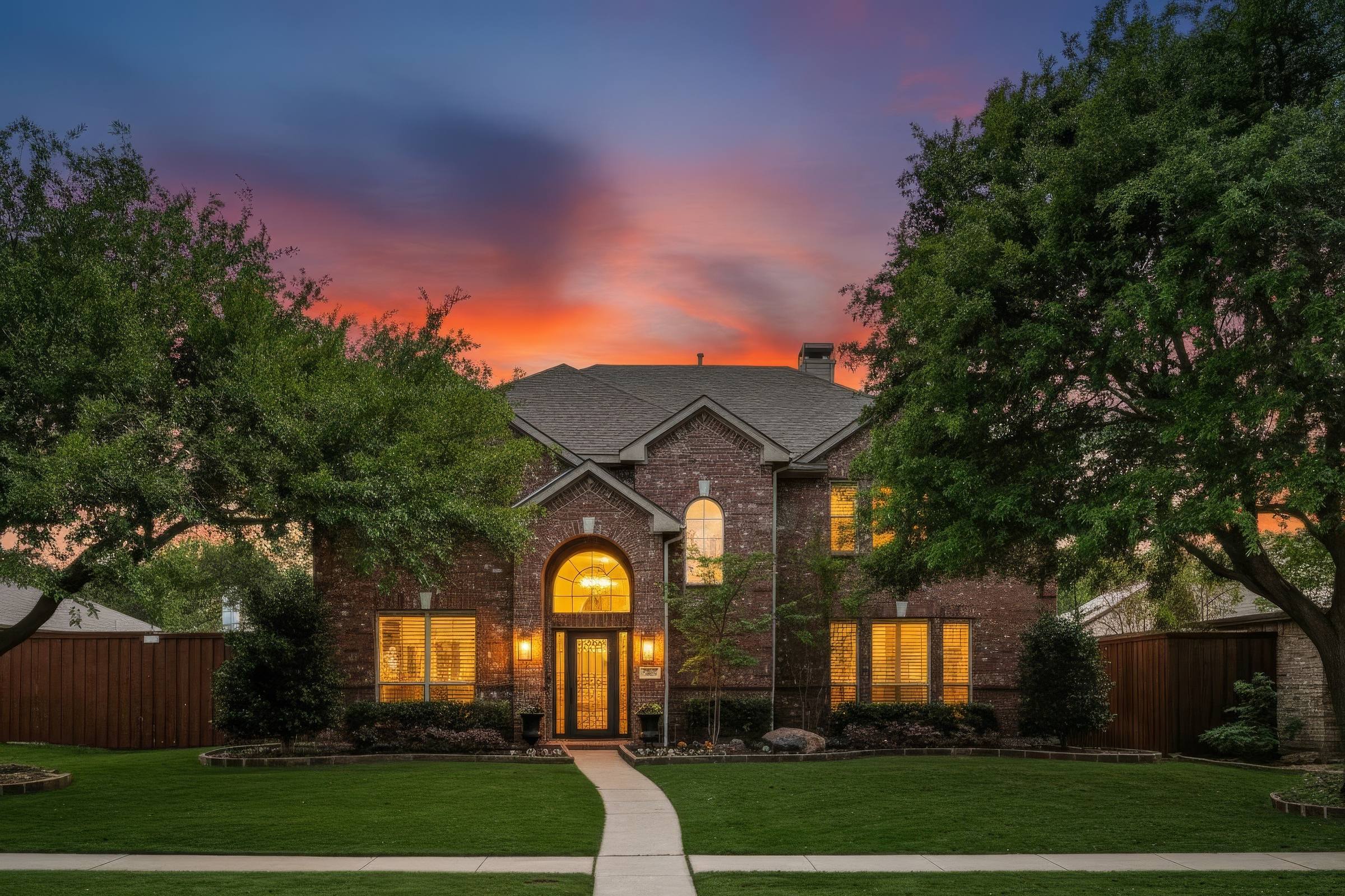 Digital twilight enhancement of a two-story brick home with glowing windows and dramatic sunset sky in Frisco, Texas