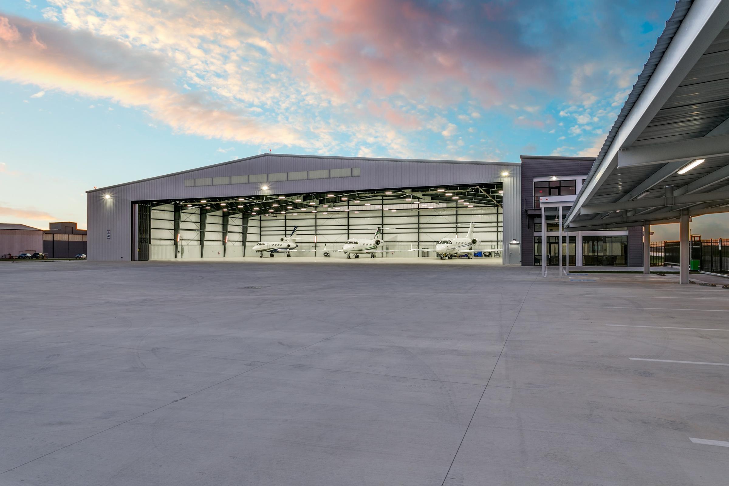 Large aviation hangar with open bay doors revealing private jets against a pastel twilight sky in Fort Worth, Texas